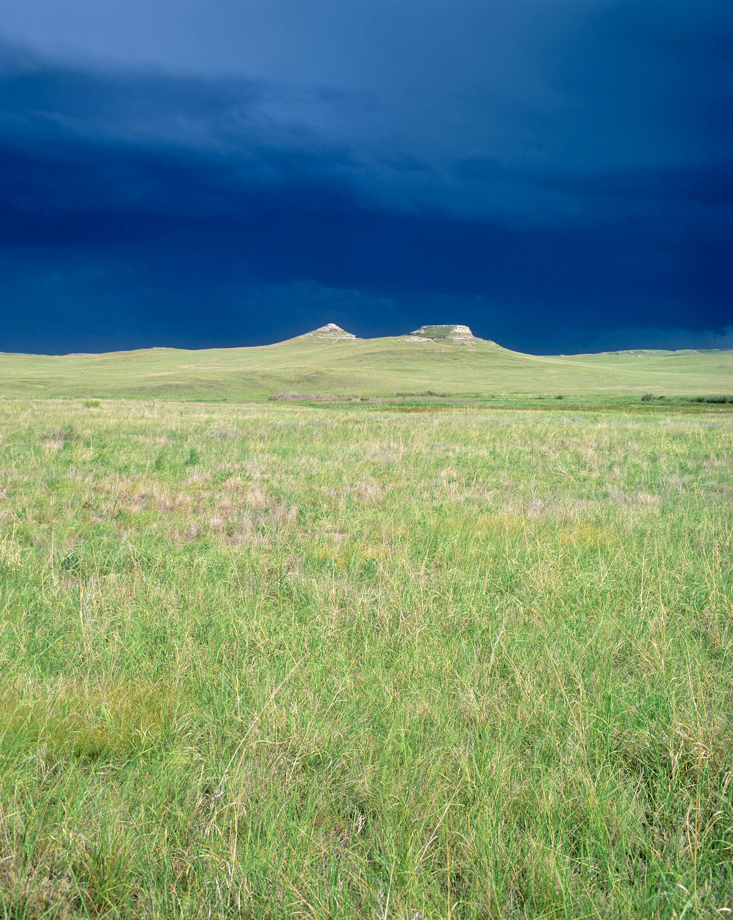 The sun illuminates the fossil hills with a dark, stormy sky in the background.