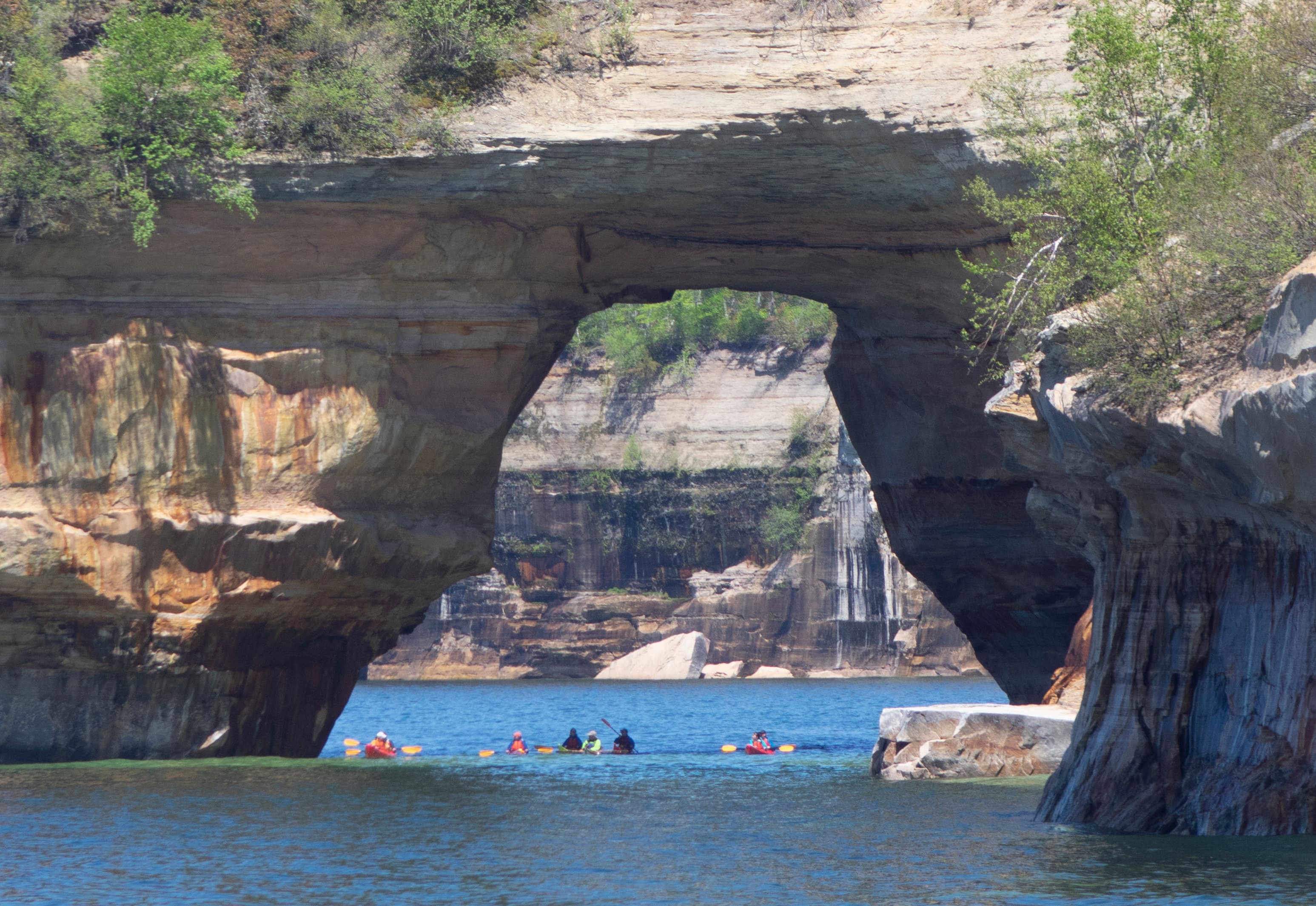 Group of kayakers under large sandstone arch