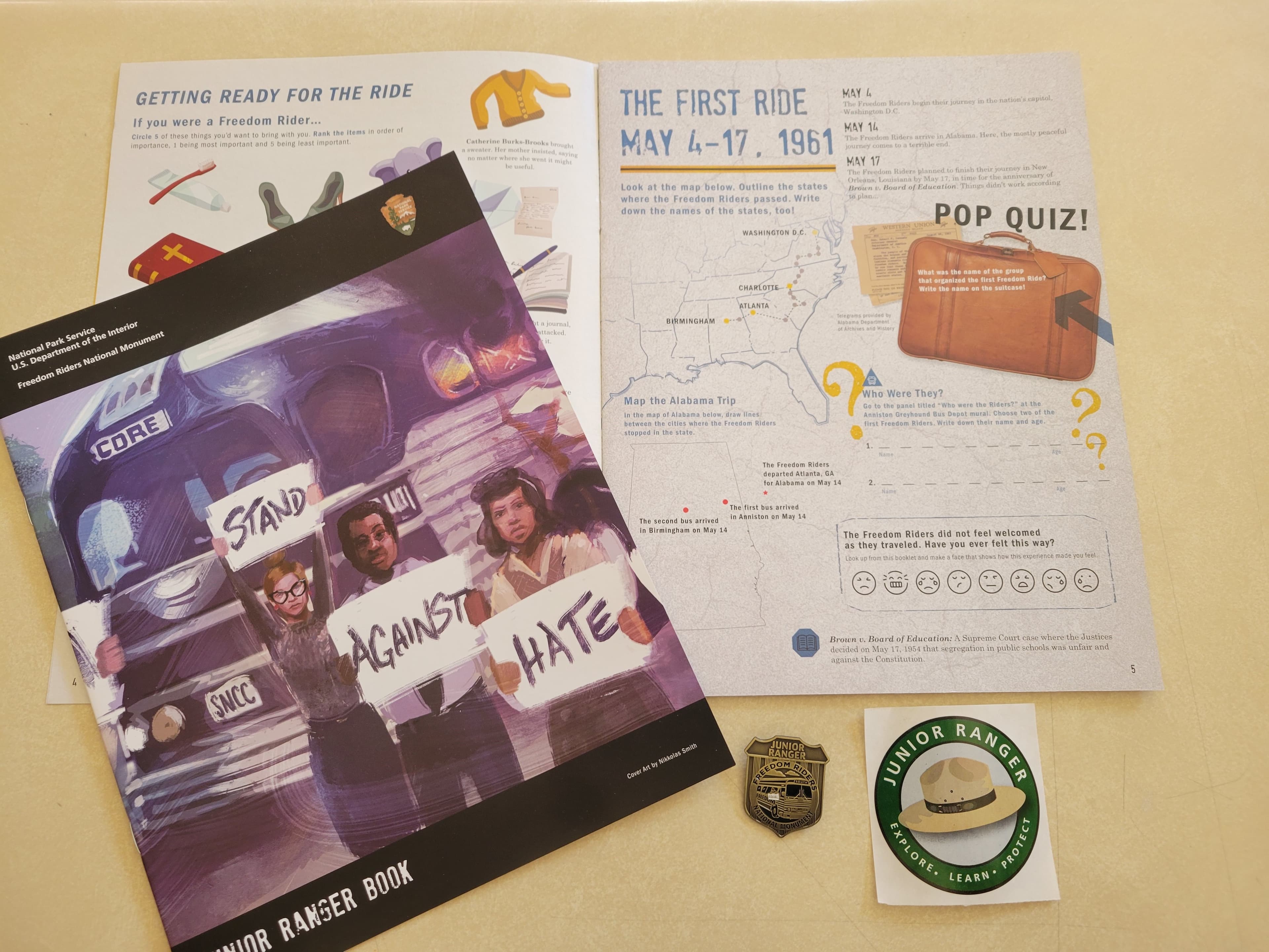 A Freedom Riders Junior Ranger book is open on a desk. Below are a Junior Ranger badge and sticker.