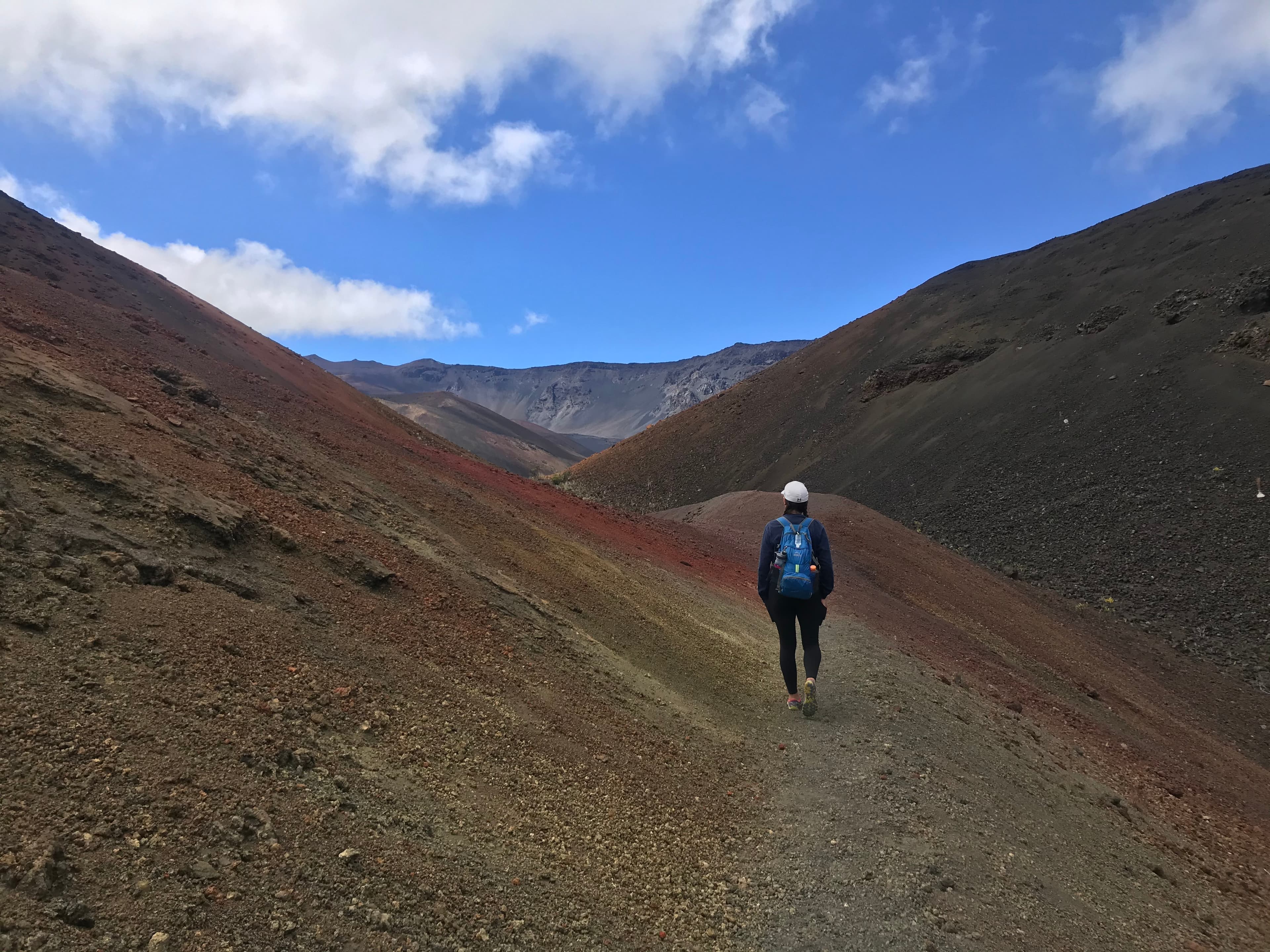 A hiker walks a trail between two red and yellow cinder cones.