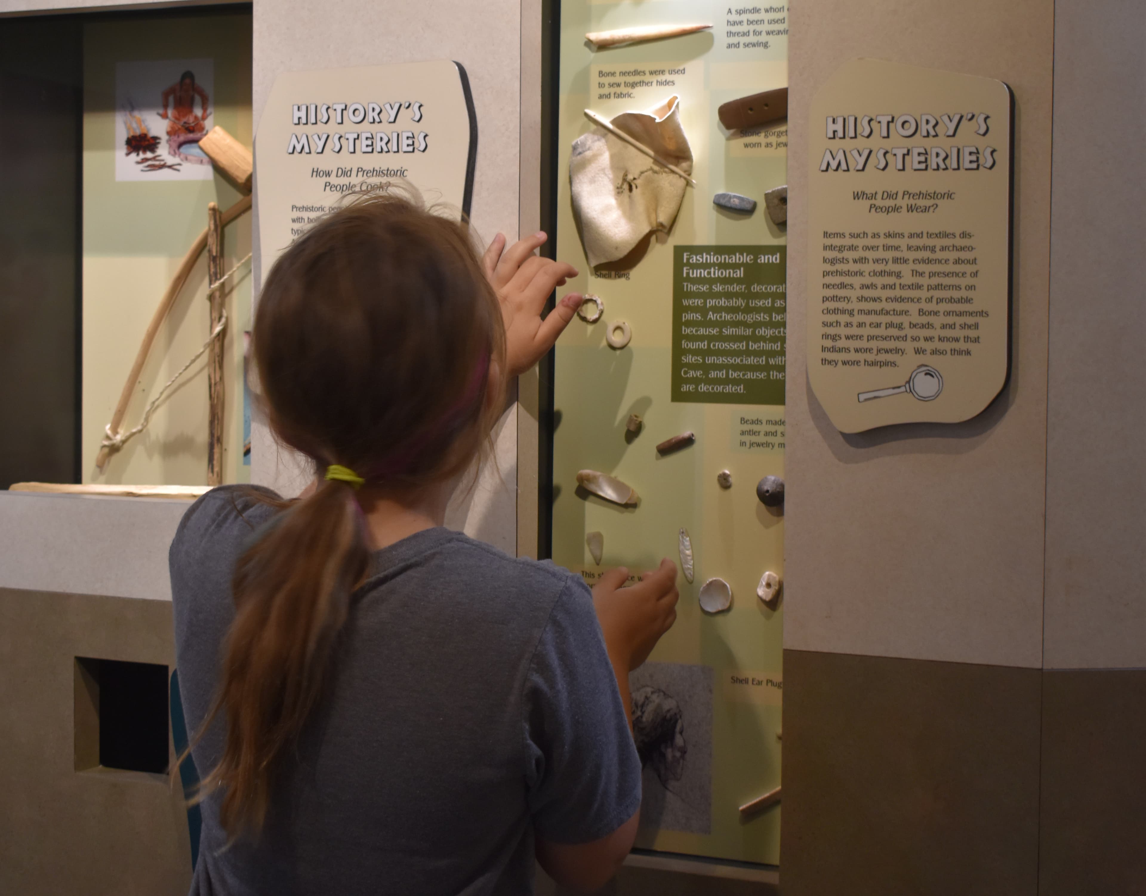 A child with long hair looks into a display of shell artifacts