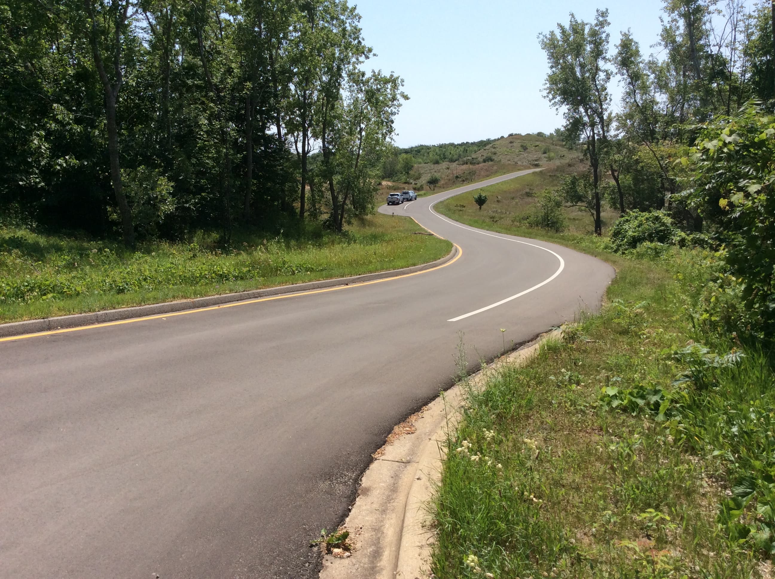 A paved road winds through plant covered sand dunes.