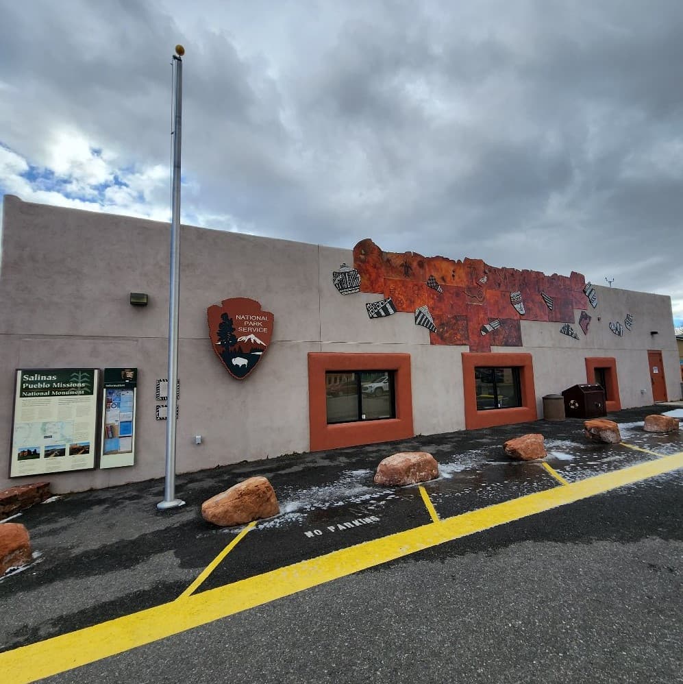 A tan building with a National Park Service arrowhead and pueblo themed artwork on the front face.