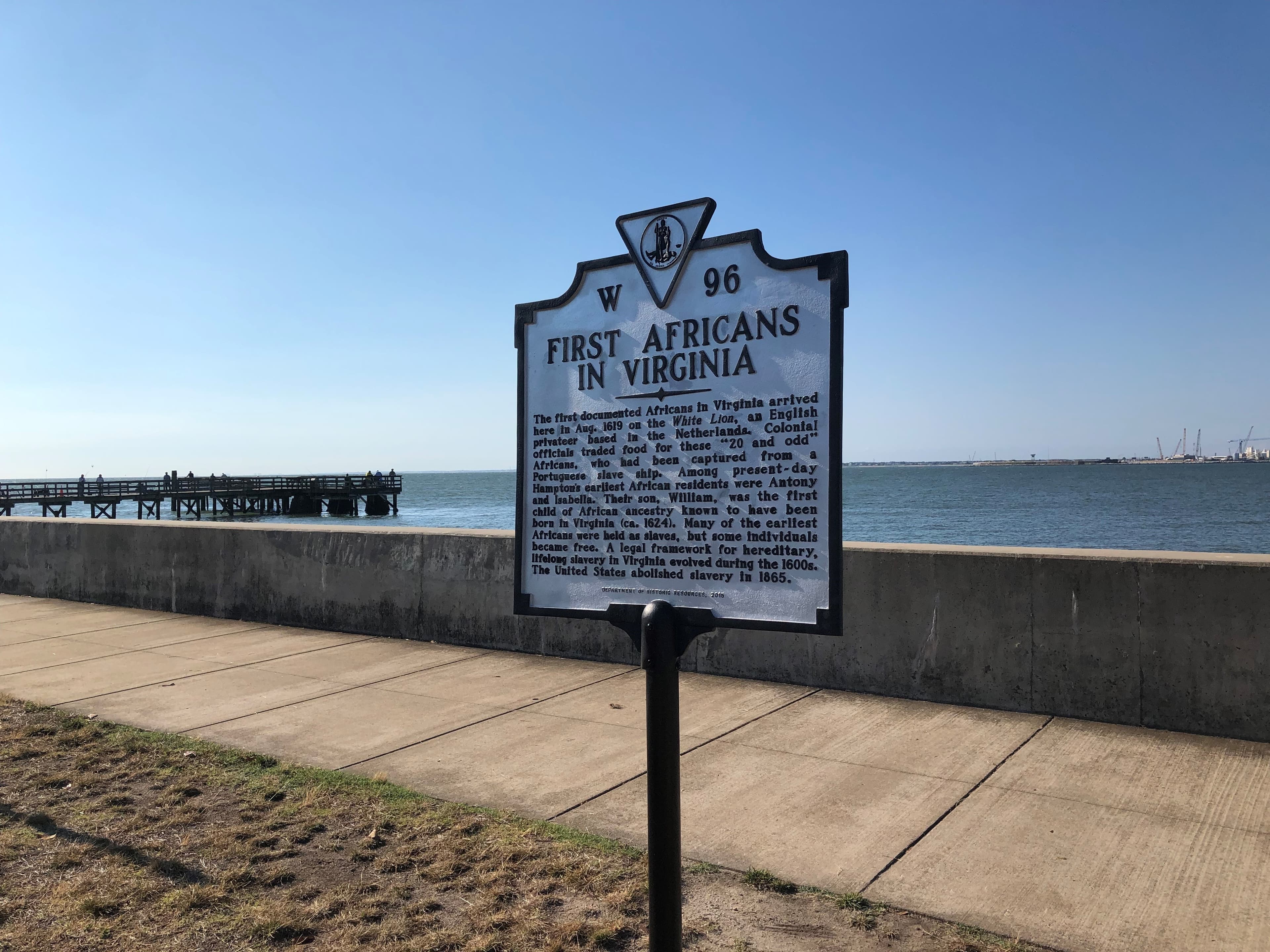 A historical marker sign on a seawall notes the arrival of the first Africans in Virginia.