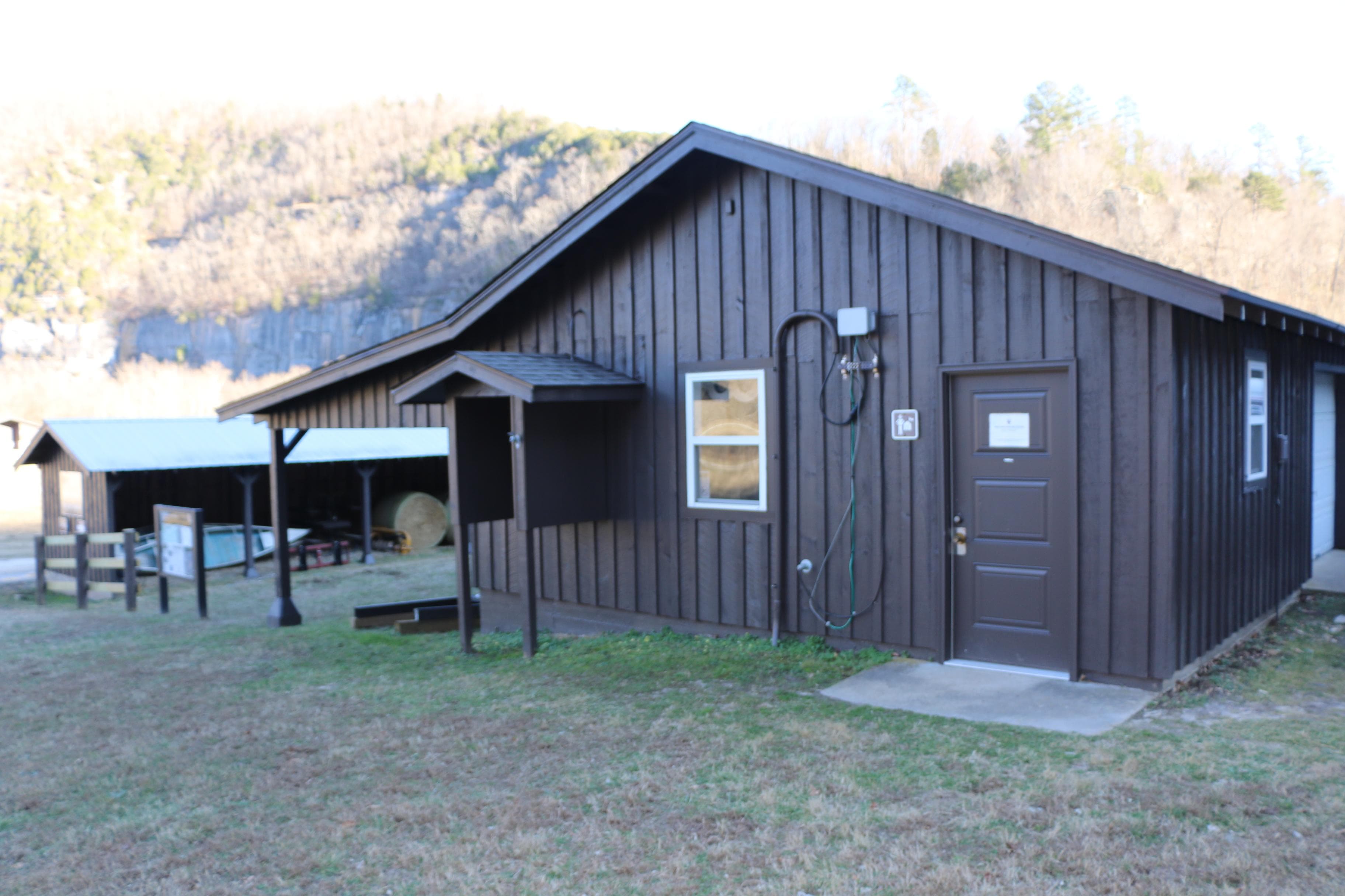 The brown Steel Creek Ranger Station sits in front of the Buffalo River and bluffs.