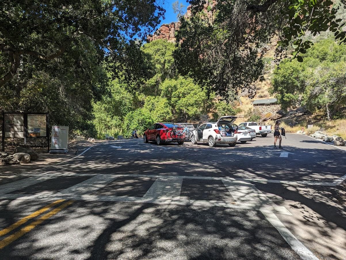 Parking area tucked near a steep rocky hillside and dirt trail that ascends gradually