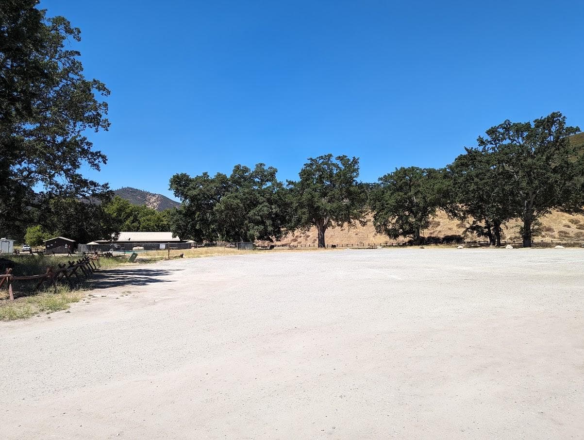 Gravel parking next to a pool and store encompassed by large Valley Oak trees
