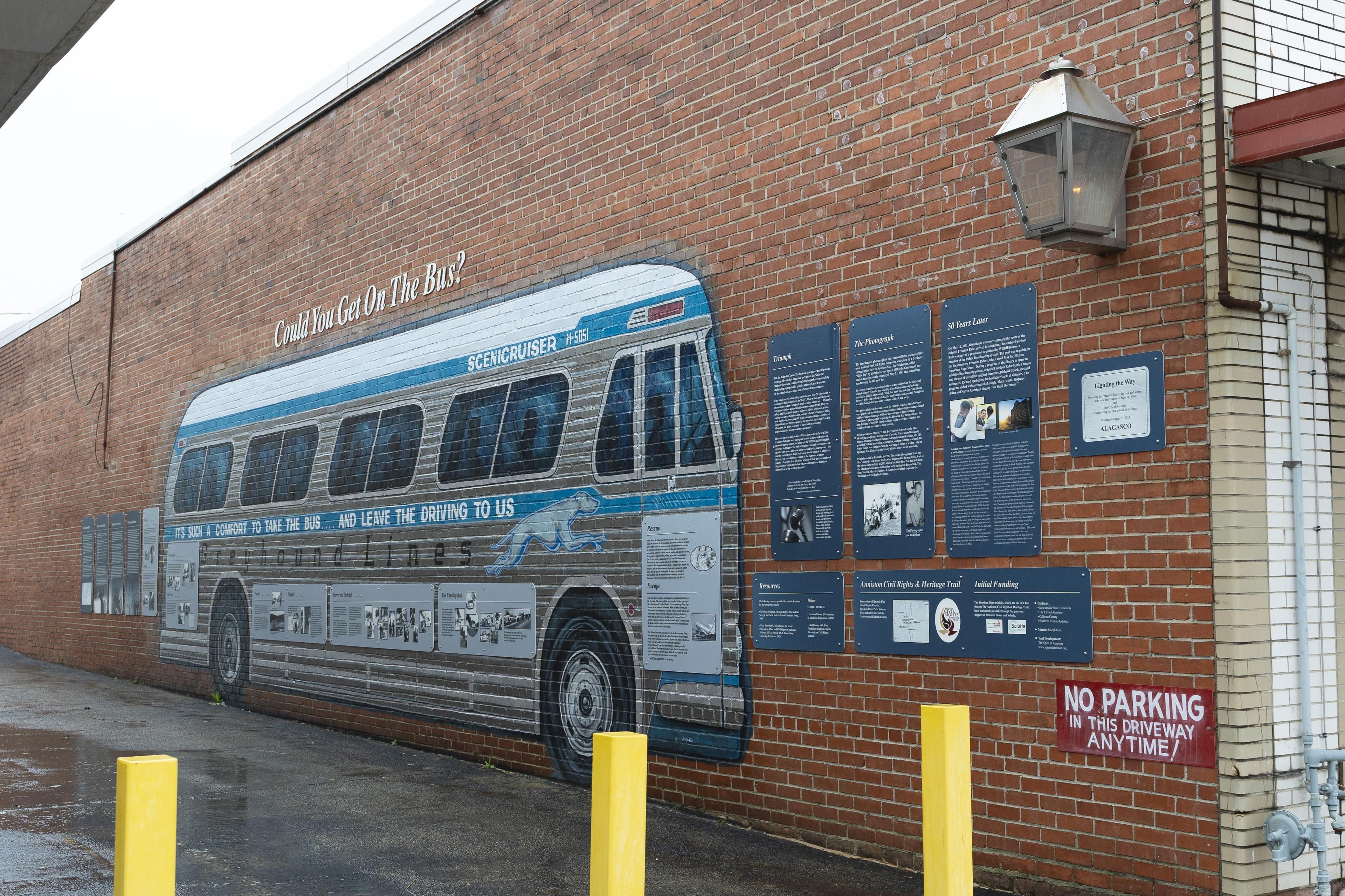 A mural of a Greyhound Bus is painted on the side of a brick building.