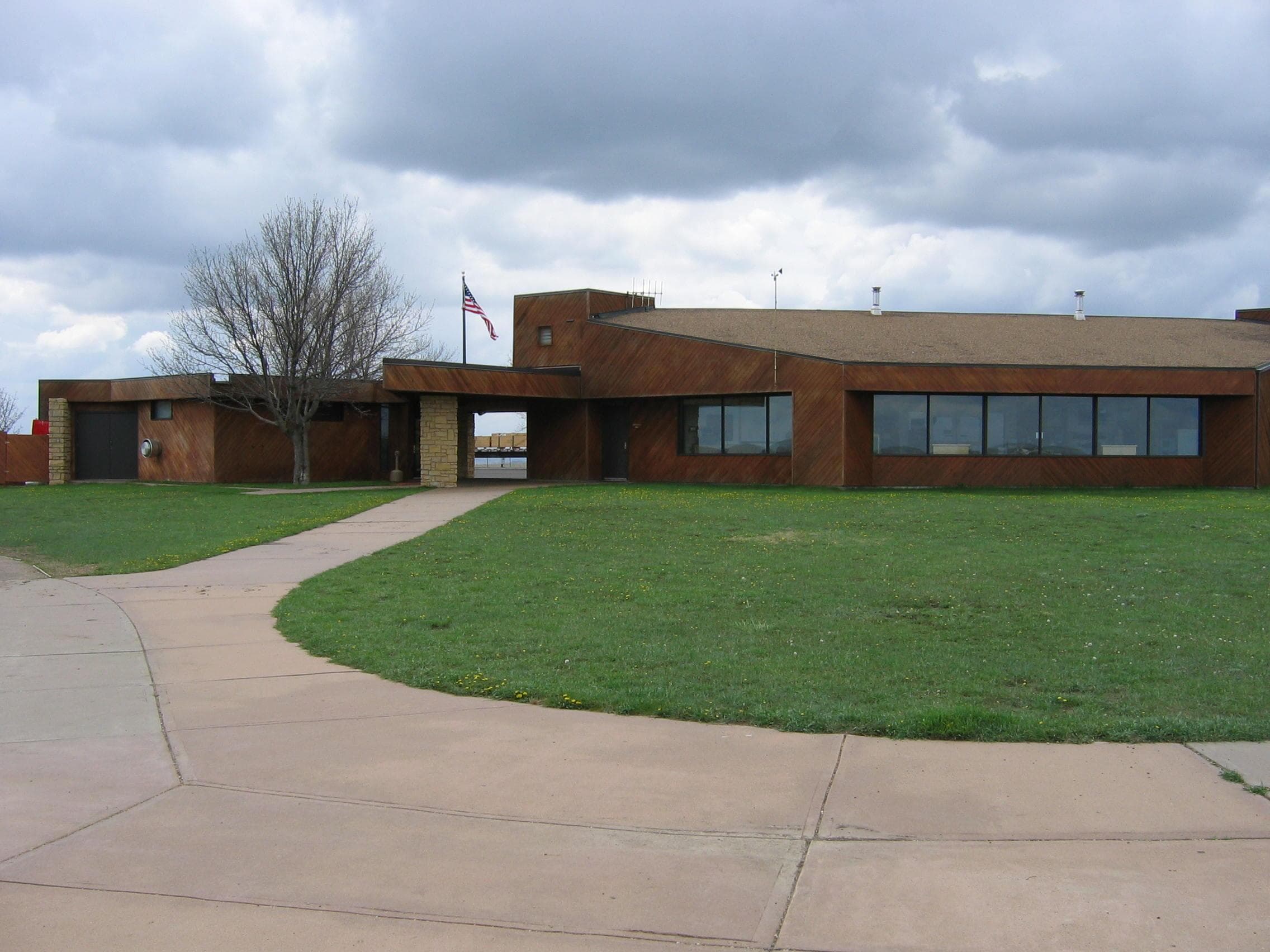 Sidewalk with green grass on either side leading to brown wooden building.