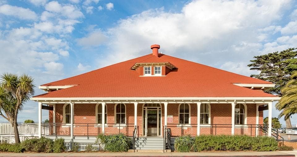 Brick building with a porch along the front and bright red roof.