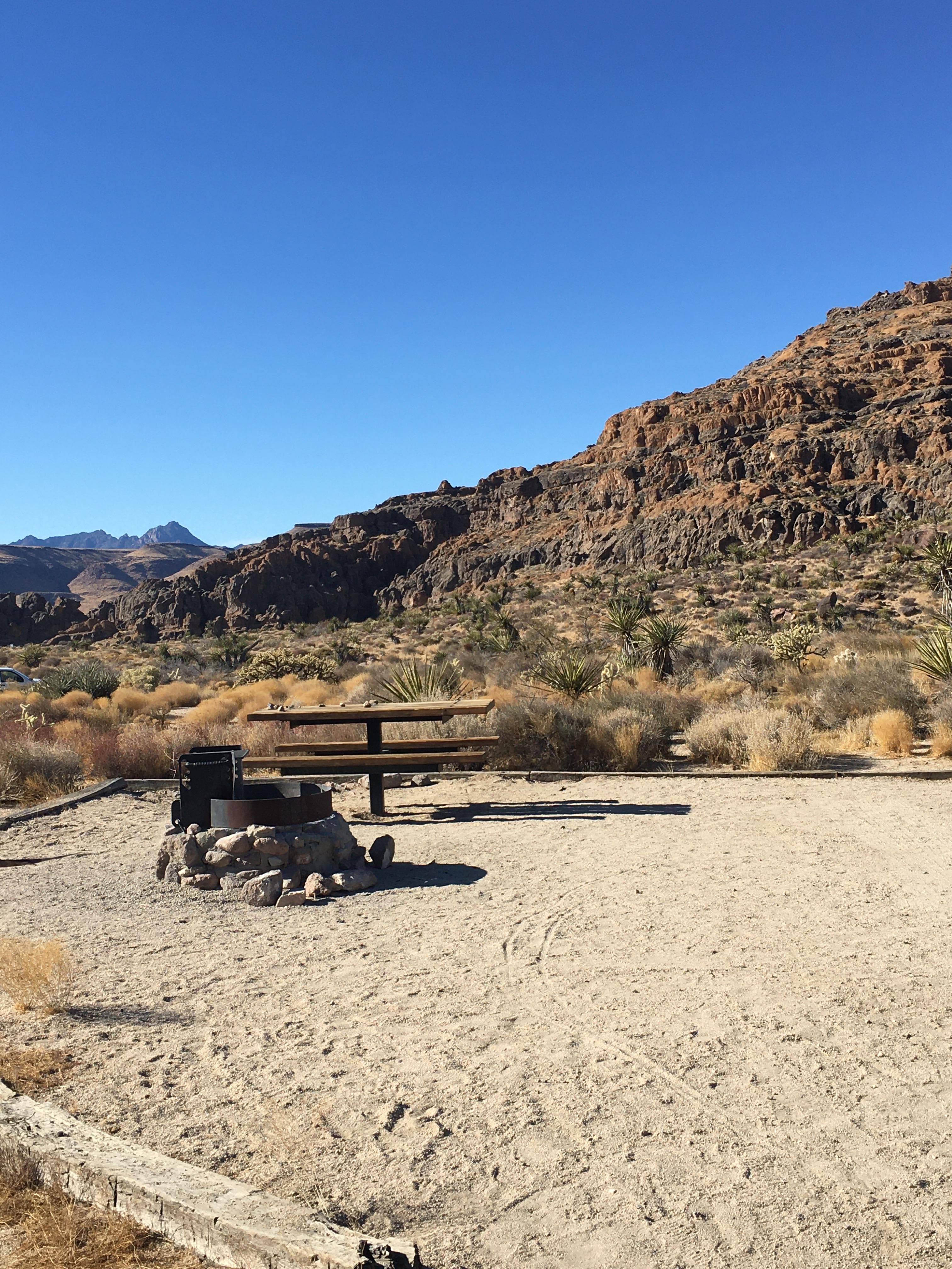 A rock fire ring and picnic table, with holey rock formations in the background