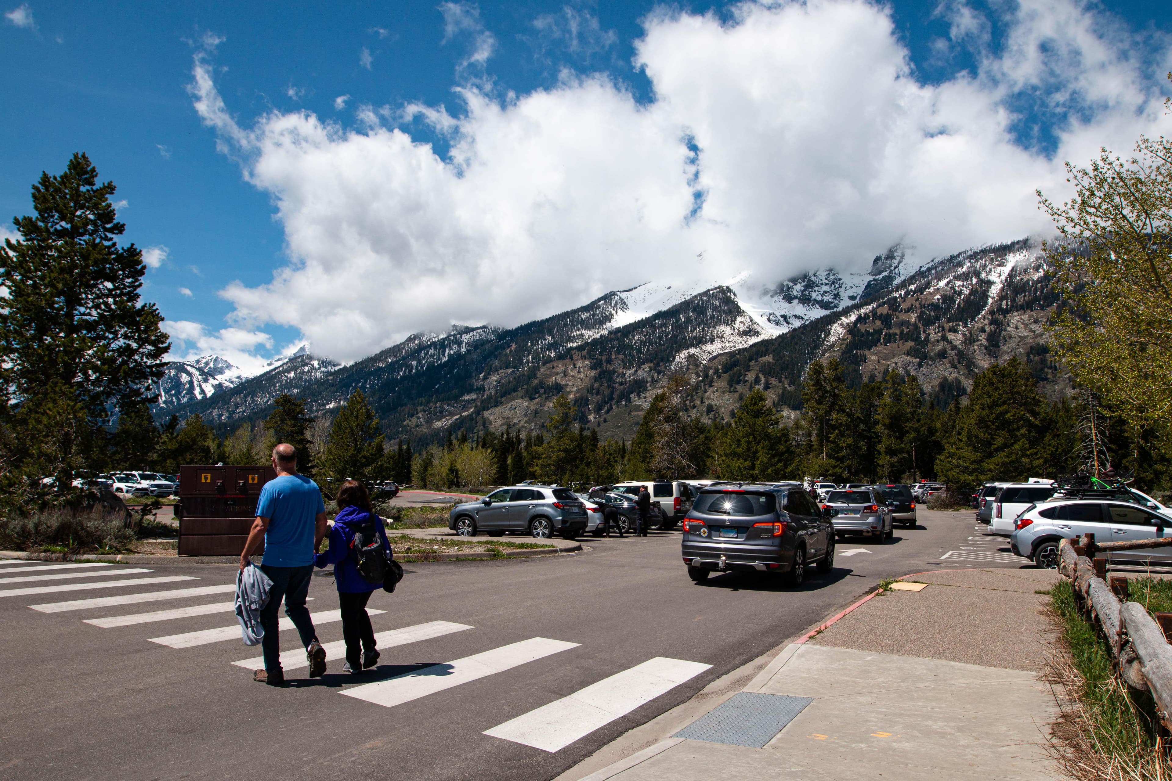 two people walk across a parking lot while cars drive behind them
