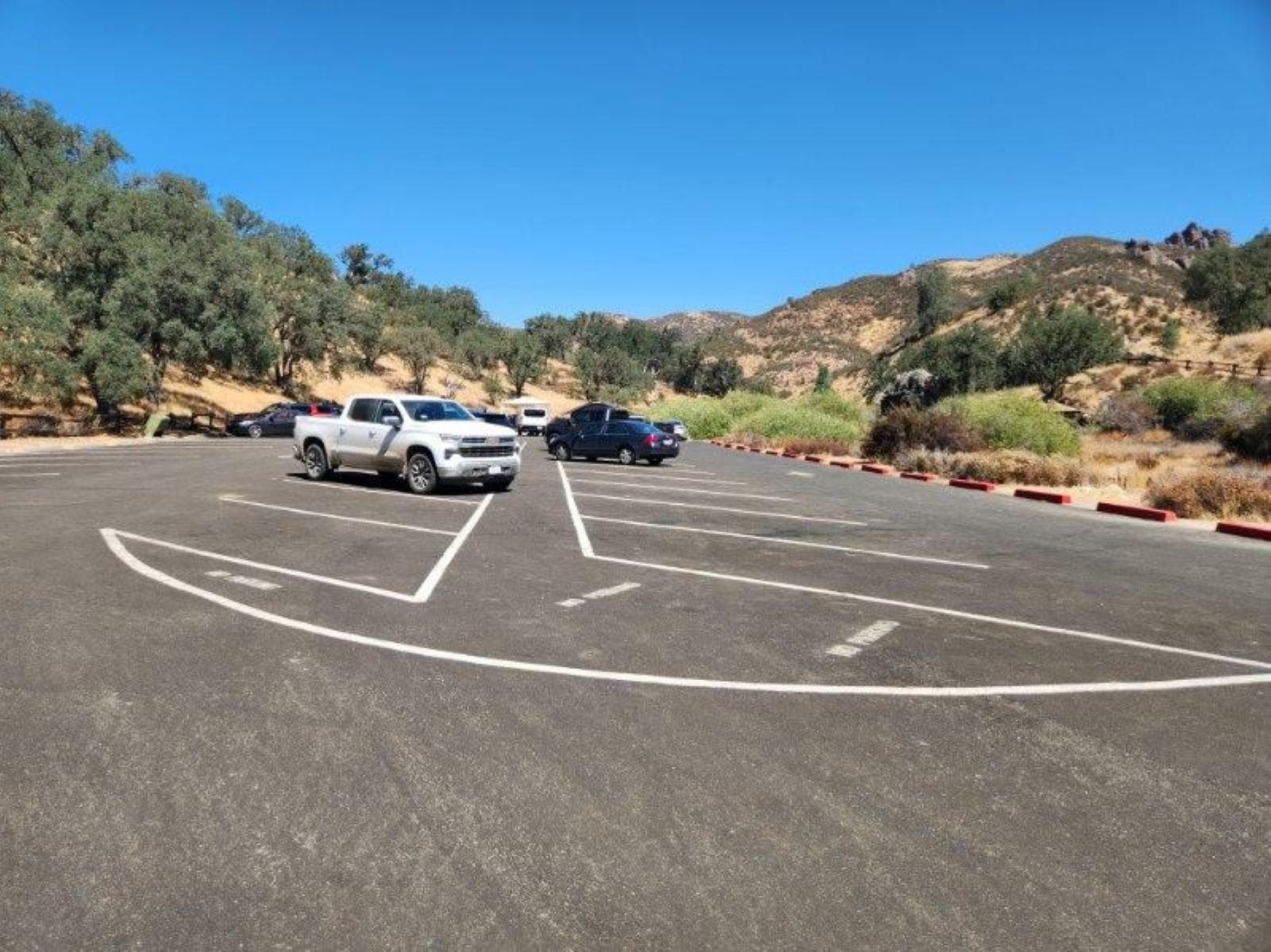 Vehicles parked in a paved parking area surrounded by chaparral covered hillsides.