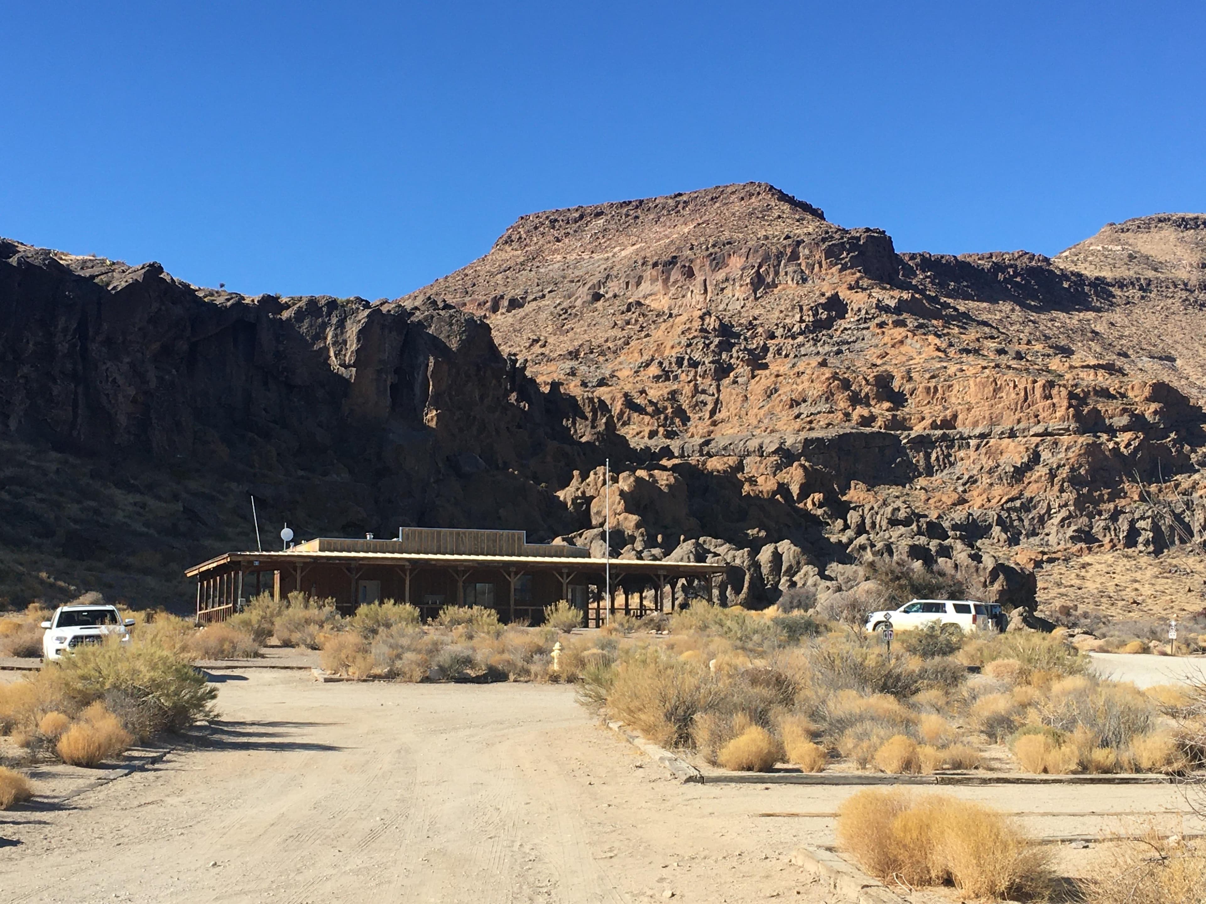 A far-away shot showing the building with massive brown hole-pocked rock formations behind it.