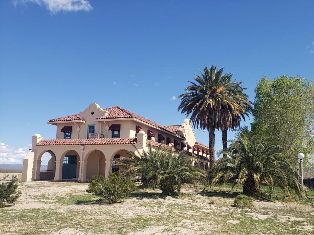 A tan building on the left, with palm trees and a green lawn in the foreground and right side.