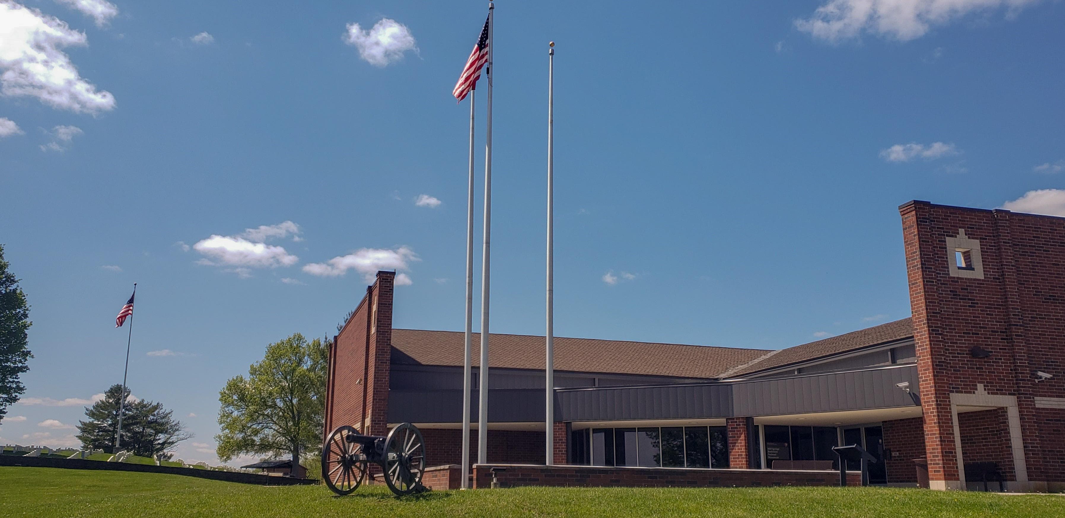 A brick building with a green lawn and flag poles.