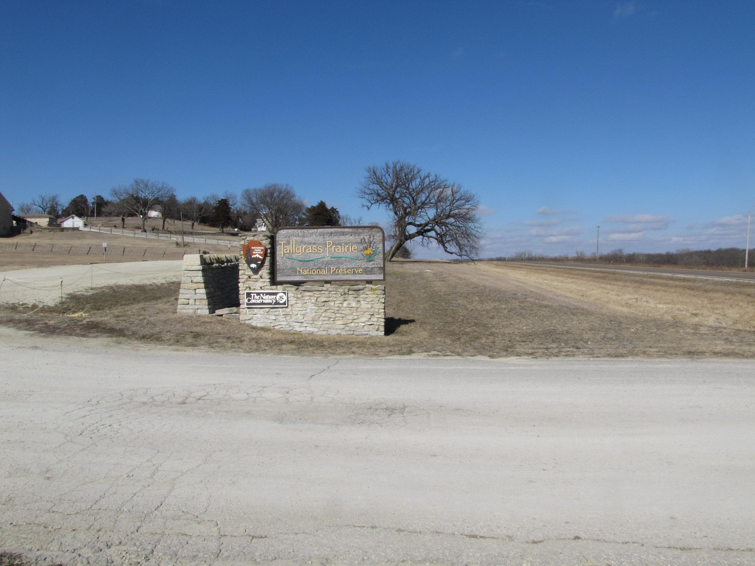 A wooden sign at the entrance of a gravel parking lot.