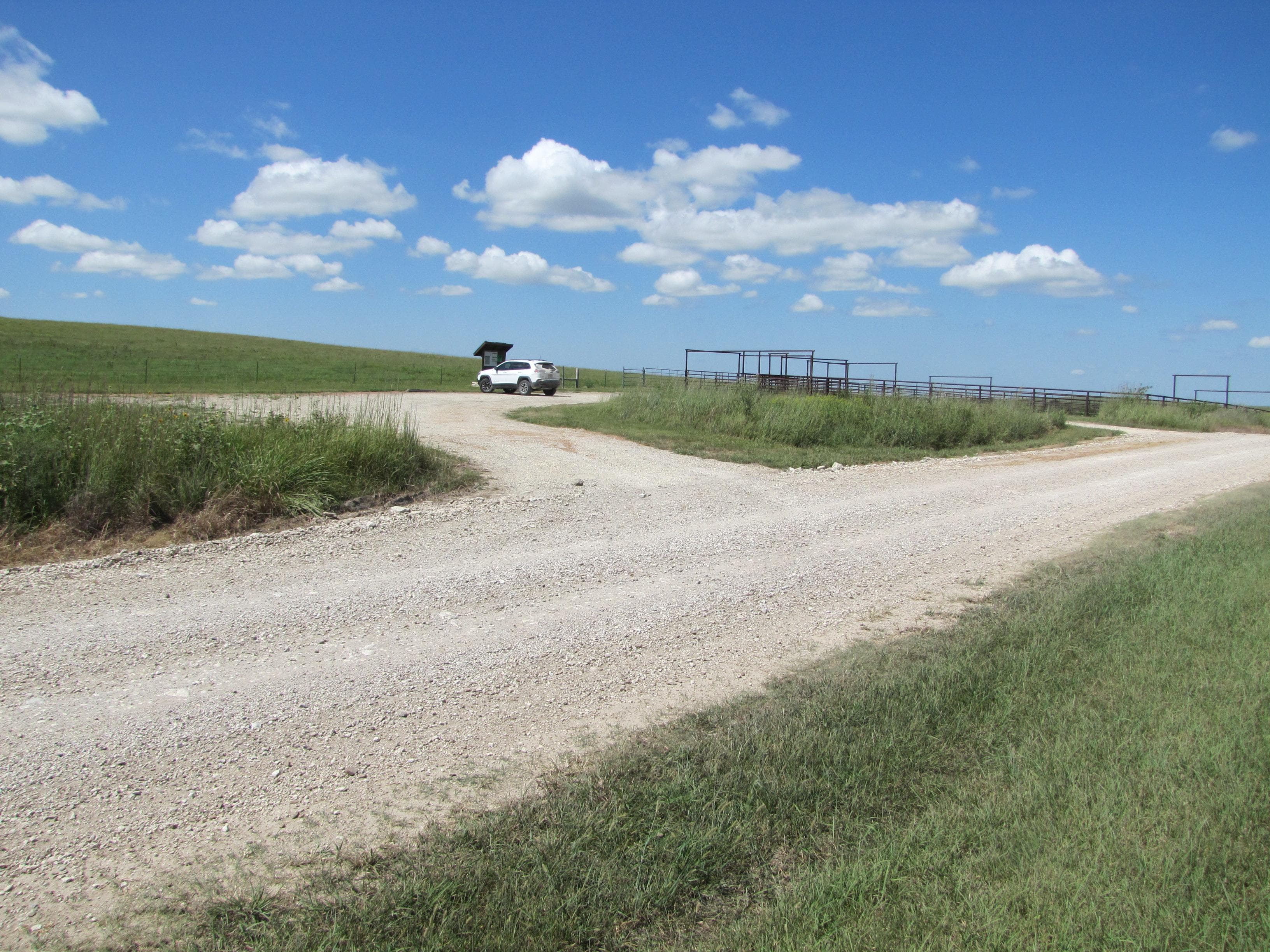 A small gravel parking lot surrounded be grass under blue sky.
