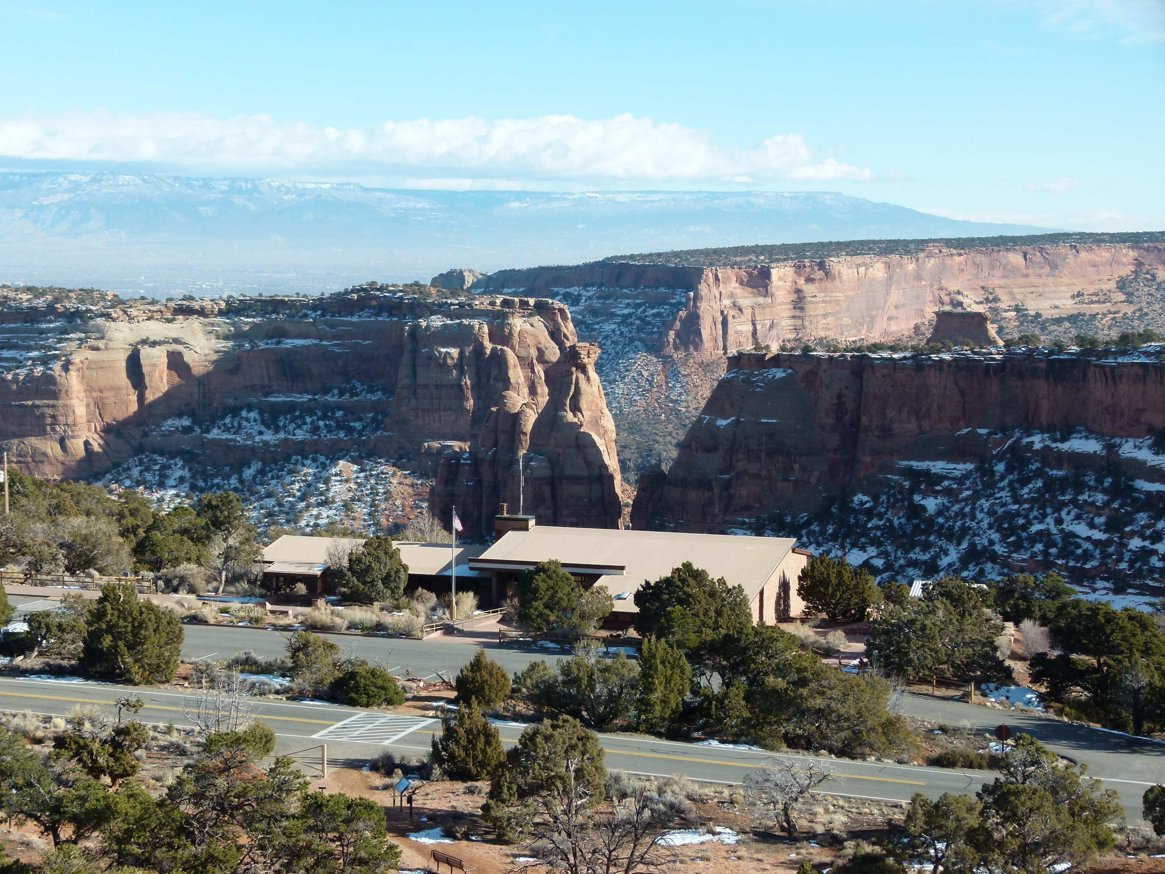 View of building with tan roof, red rock canyons in background, mountains in far distance