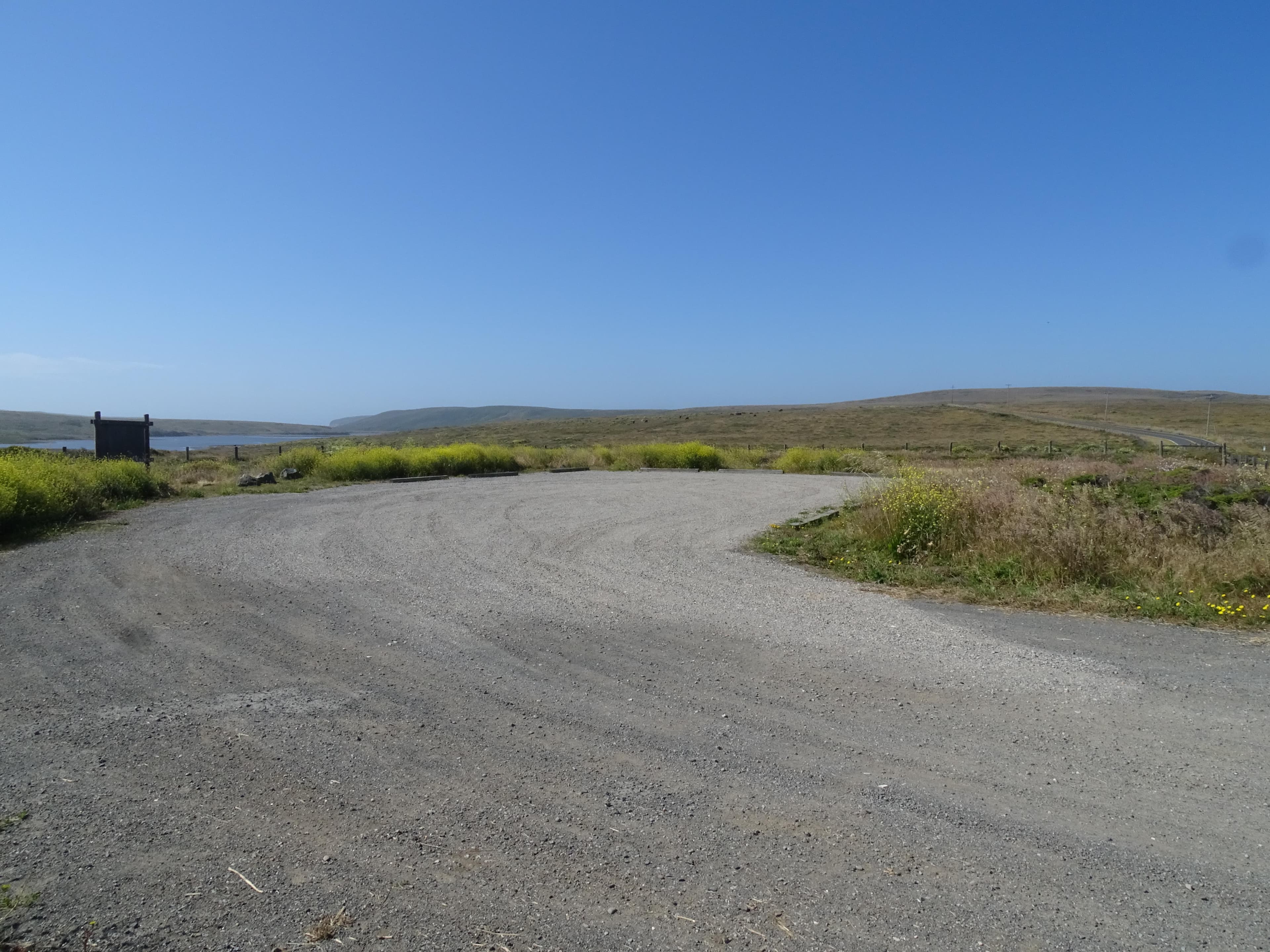 A small gravel parking lot surrounded by pastureland. A large brown sign board is on the left.