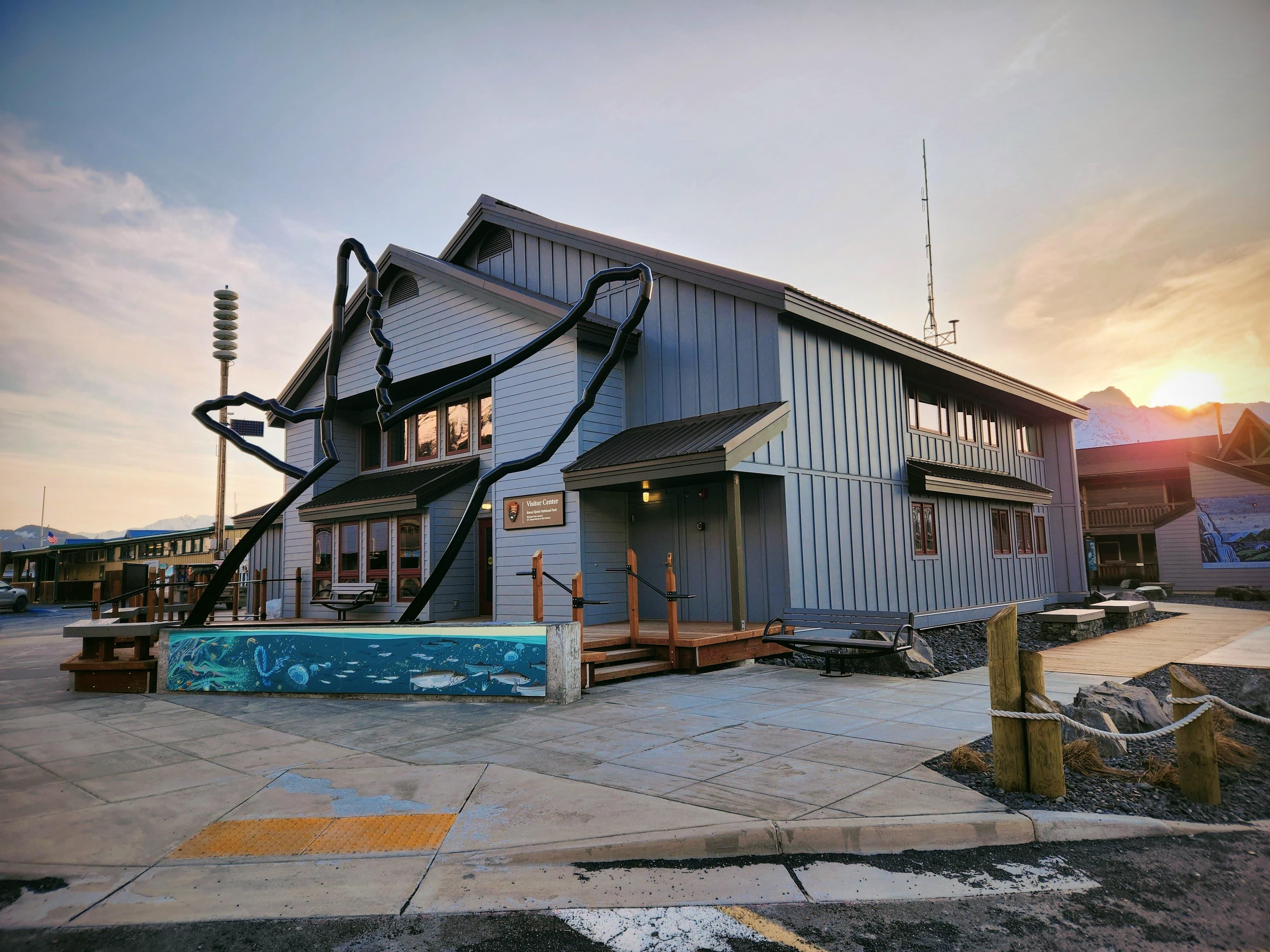 A grey building with humpback whale outline statue with sunrise in the background.