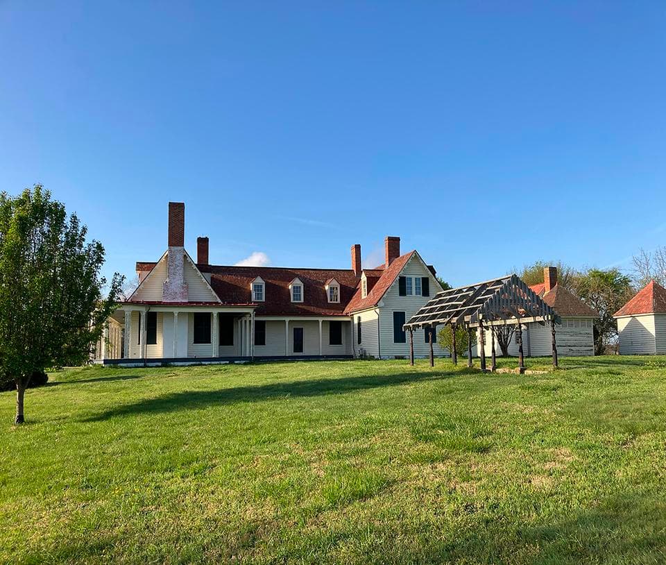 White two-story house with a red roof in the background and a green lawn in the foreground.
