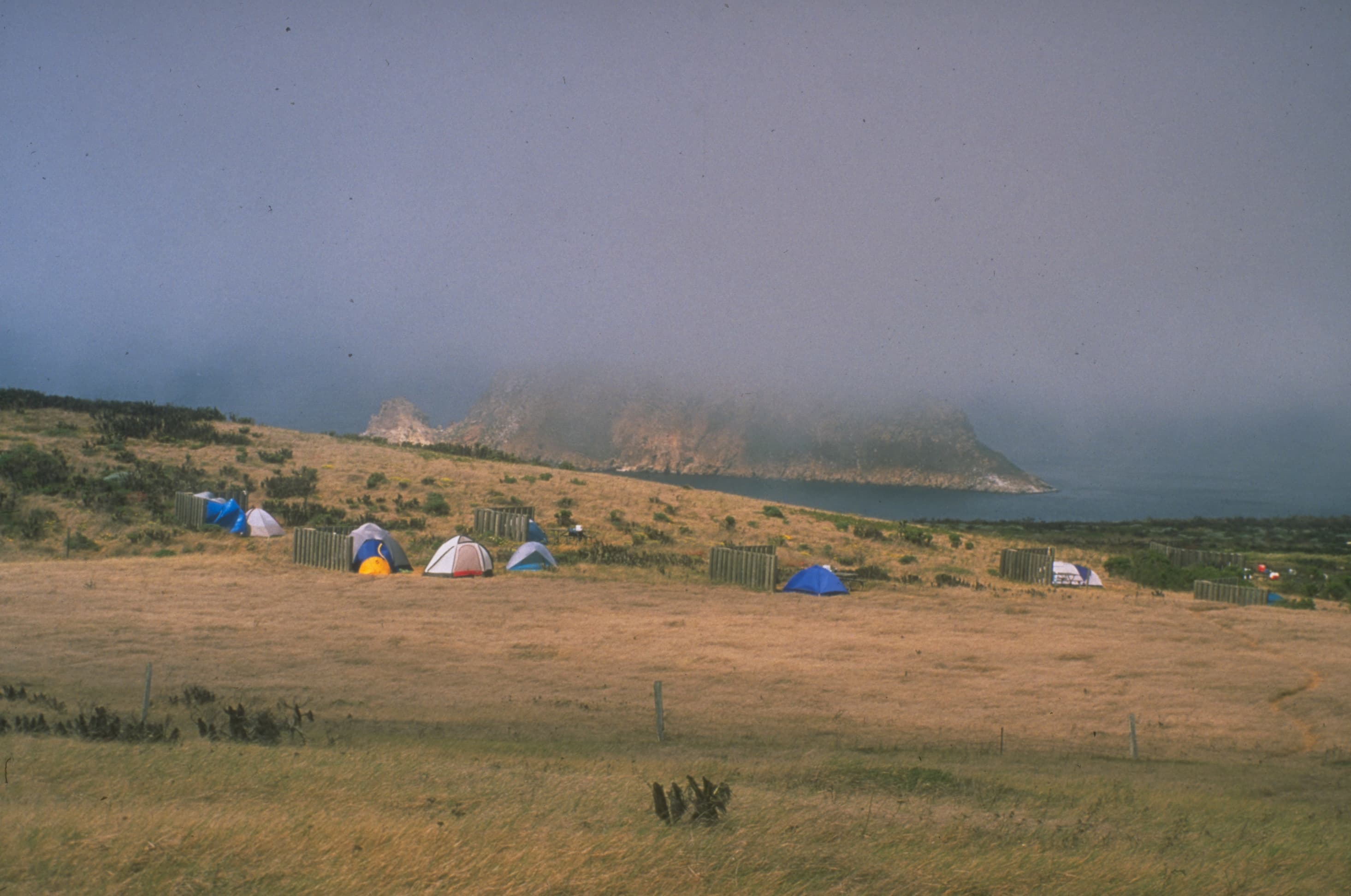 Camping tents in grassland overlooking a foggy ocean.