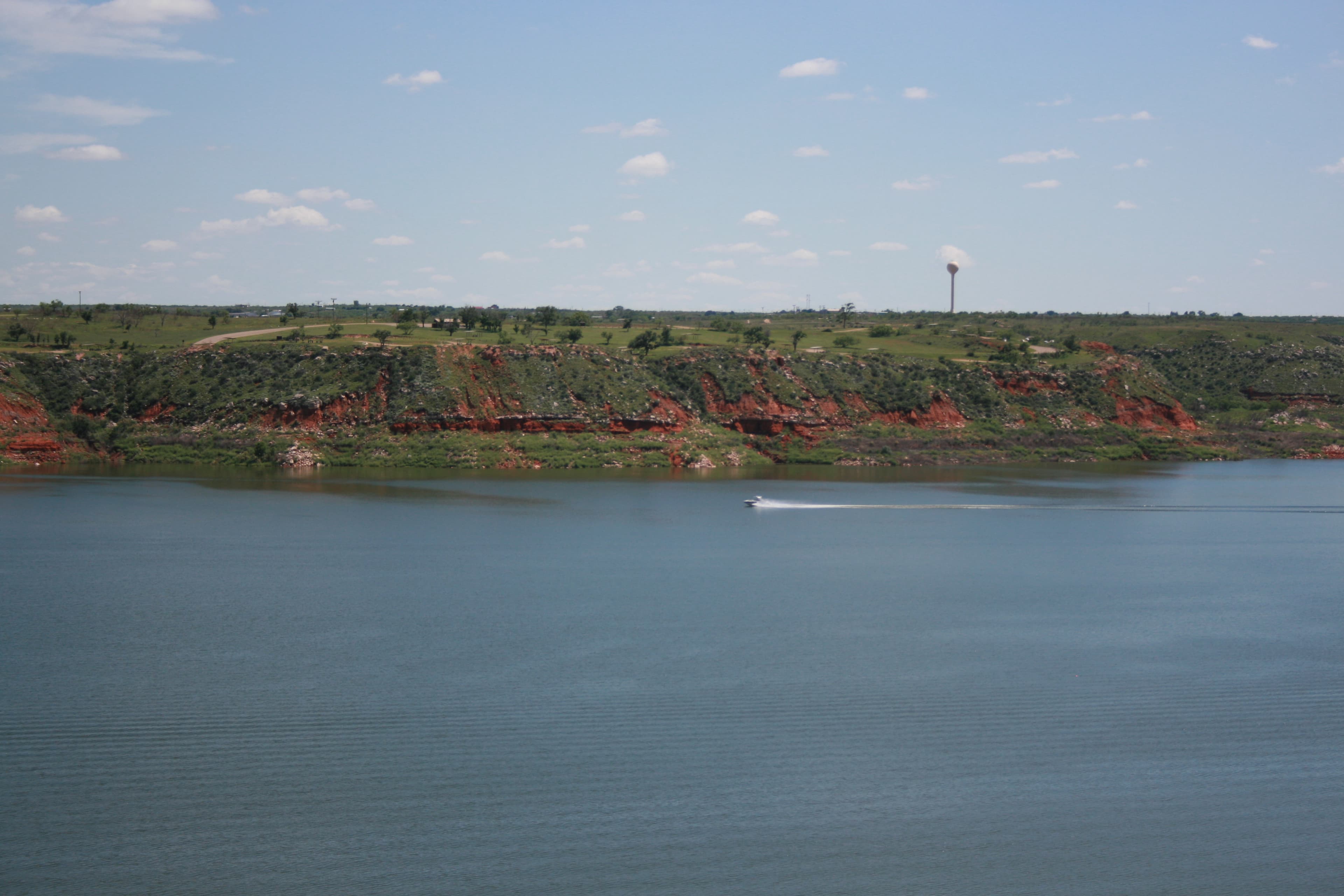 A boat travels across Lake Meredith on a sunny day. The lake is light blue.