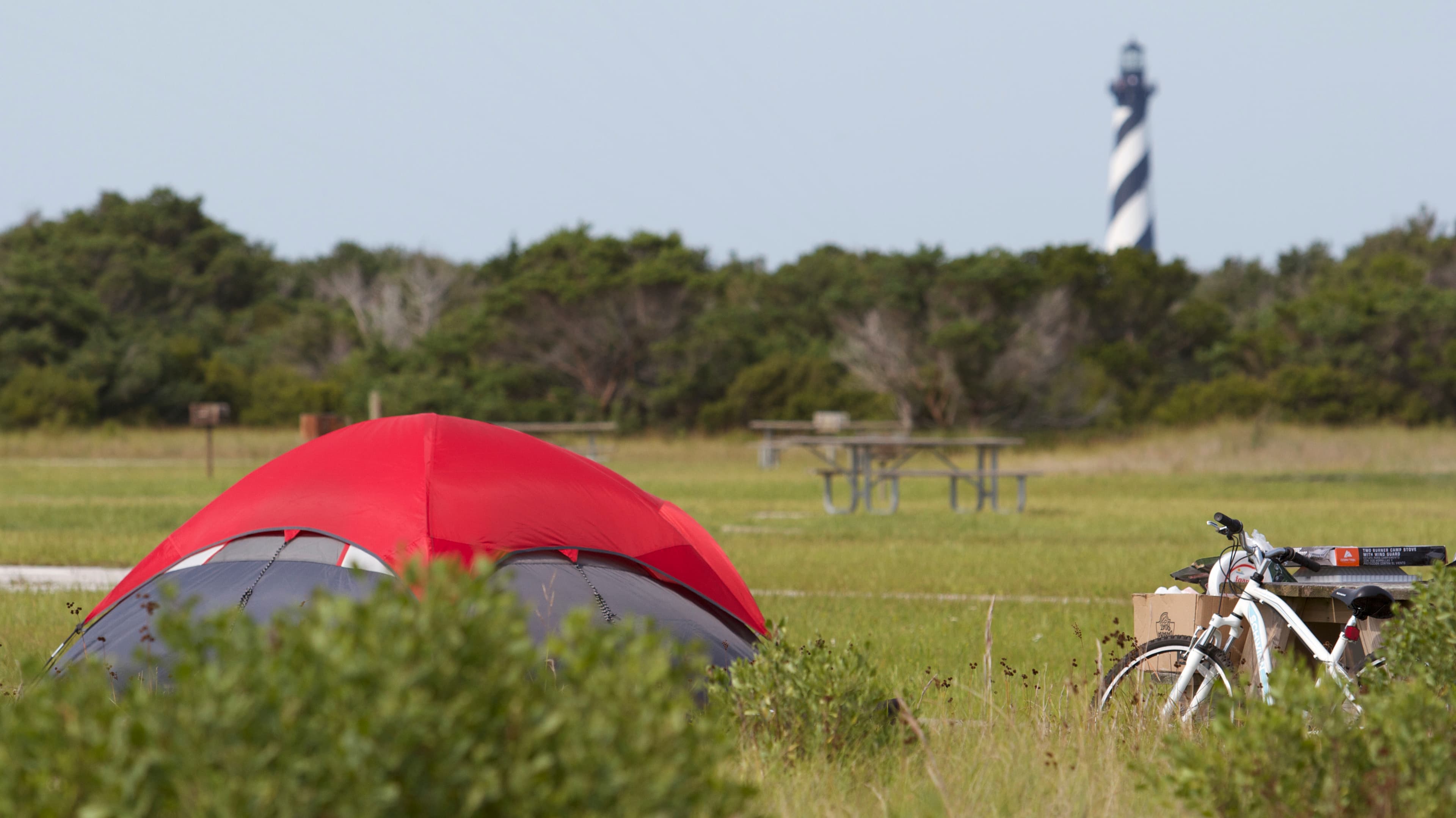 Red tent and bicycle at a camp site with the Cape Hatteras Lighthouse in the background.