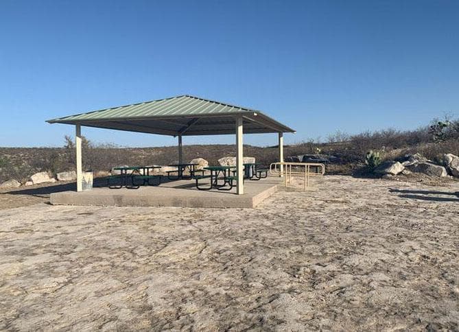 Tin-roofed pavilion with cement floor and accessibility ramp surrounded by flat ground.