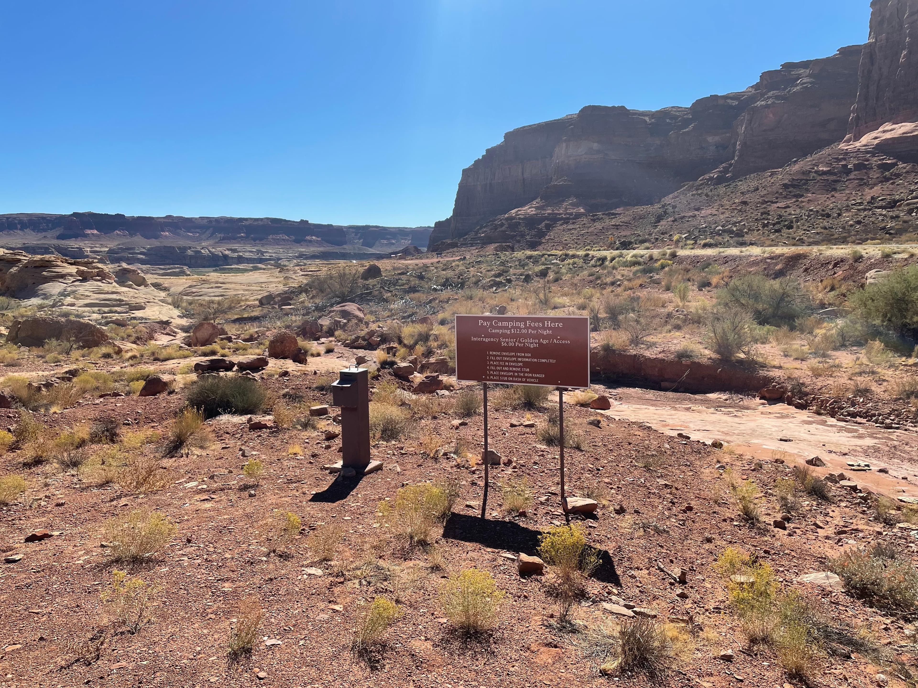 A rocky desert landscape. A stout metal post with a slot in the top is next to a sign: Pay camping F