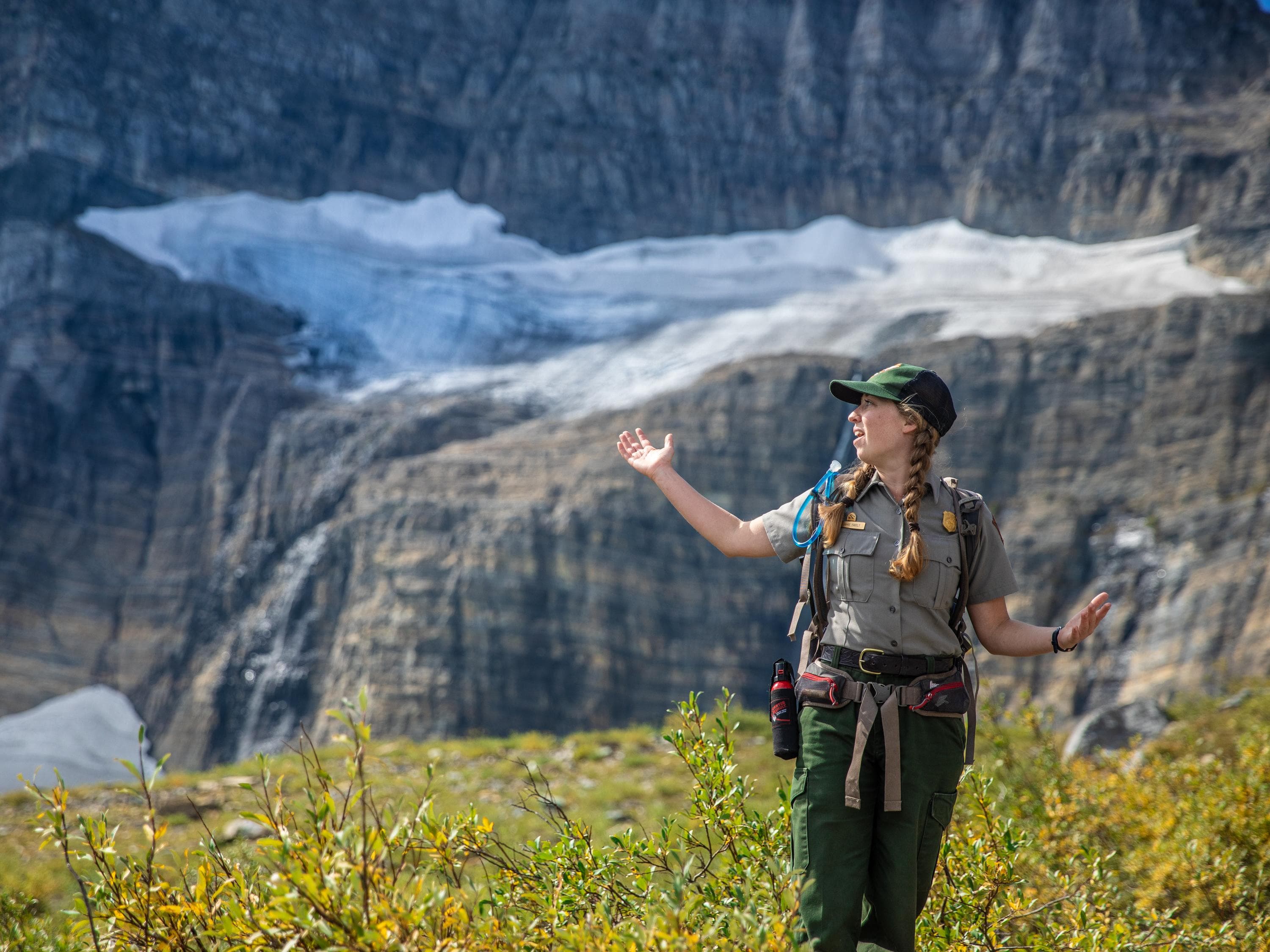 A park ranger standing with arms out in front of snow and ice.