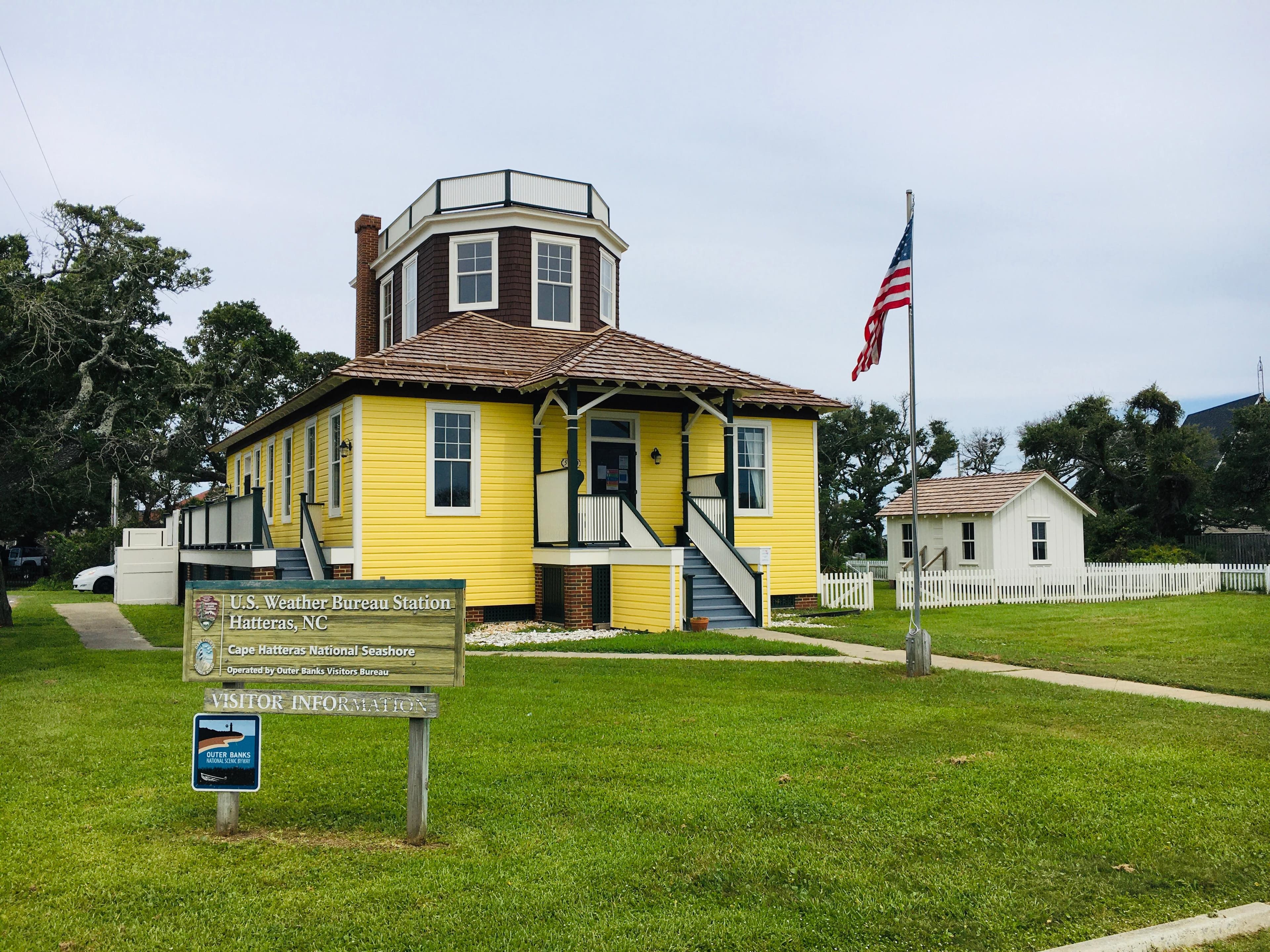 A yellow building with a brown roof and an American Flag