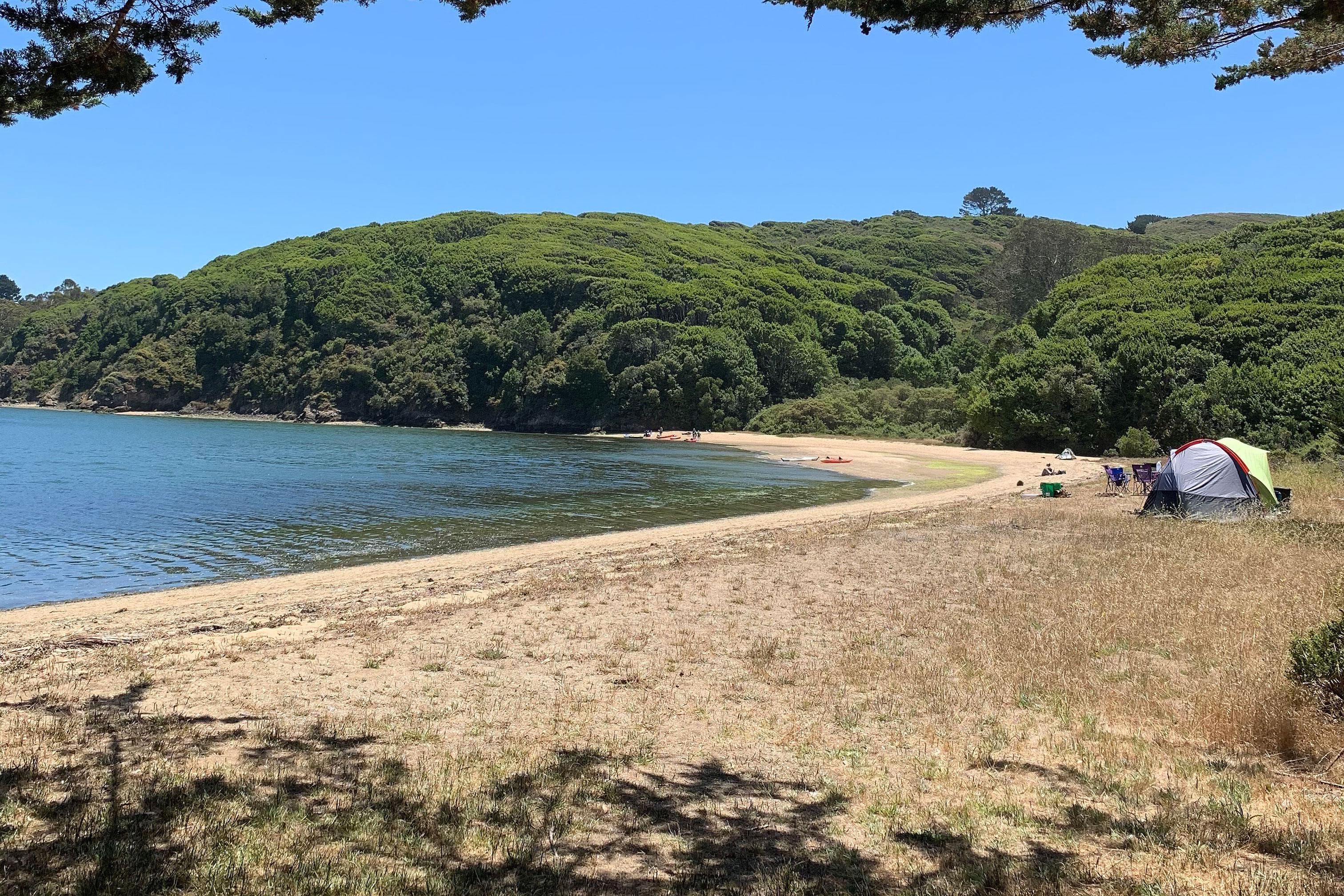 A small tent is set up above a sandy beach that bends to the left in the distance.