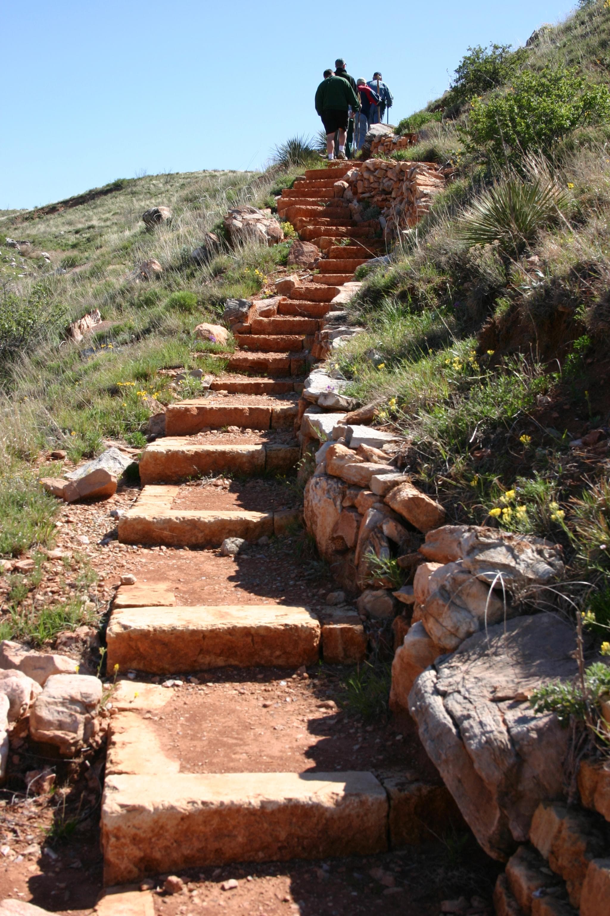 A handful of hikers at the top of a grassy hill with a long set of red stone steps