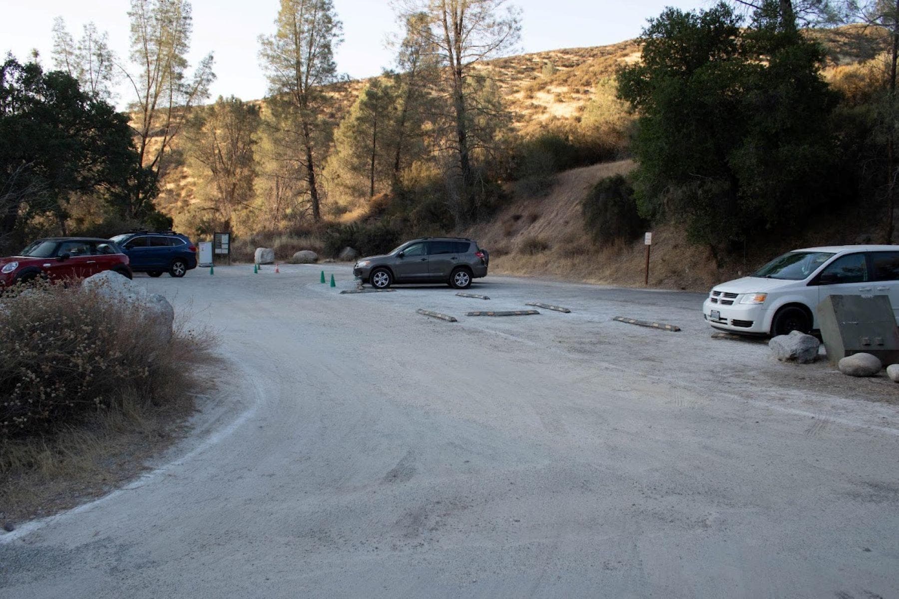 Gravel parking area situated next to a hillside blanketed with shrubs, blue oak, and grey pine trees