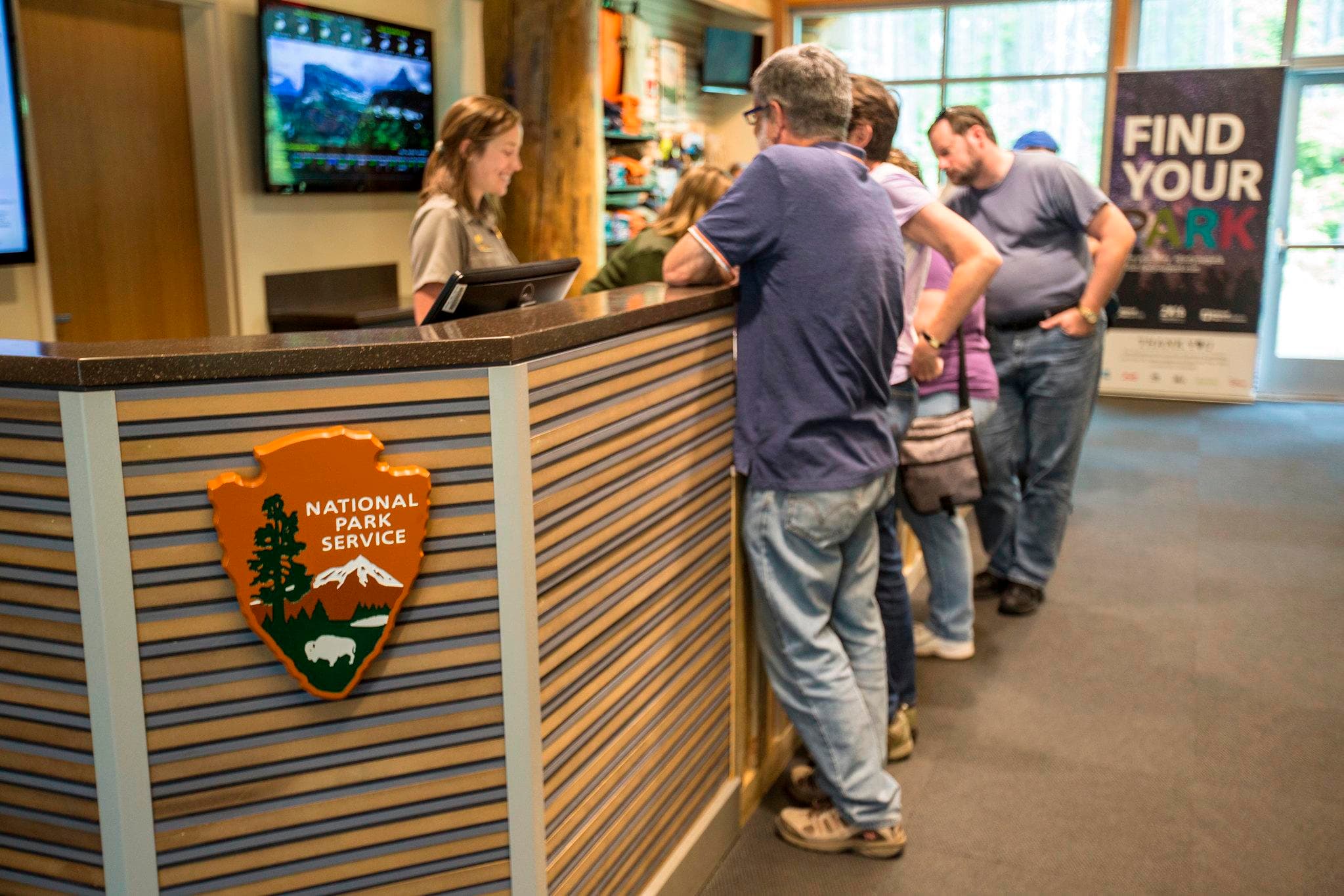 A park ranger, standing behind an information desk, assists a group of visitors.