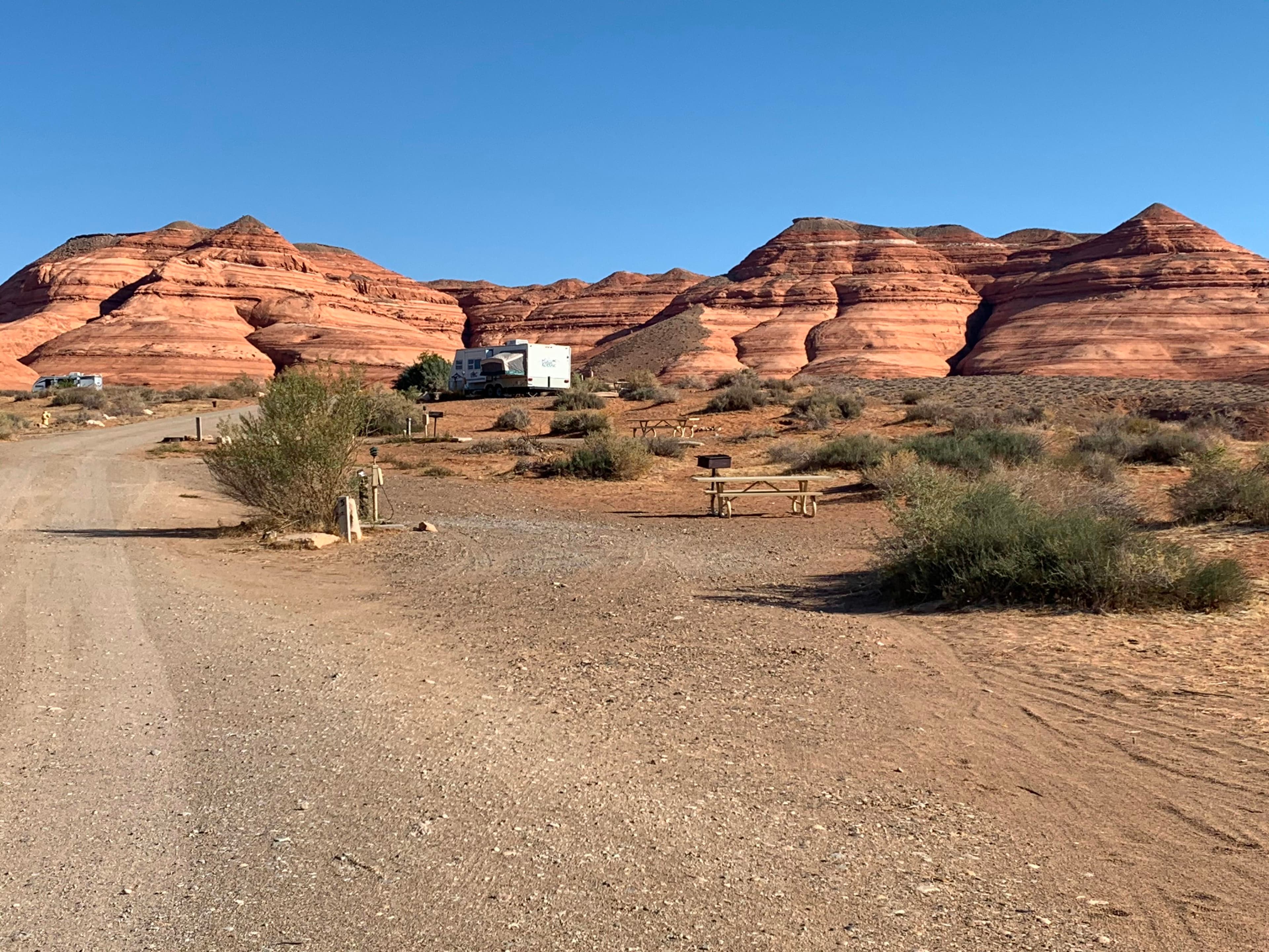 Gravel road with camping sites that have picnic tables, grills, hookups, two RVs