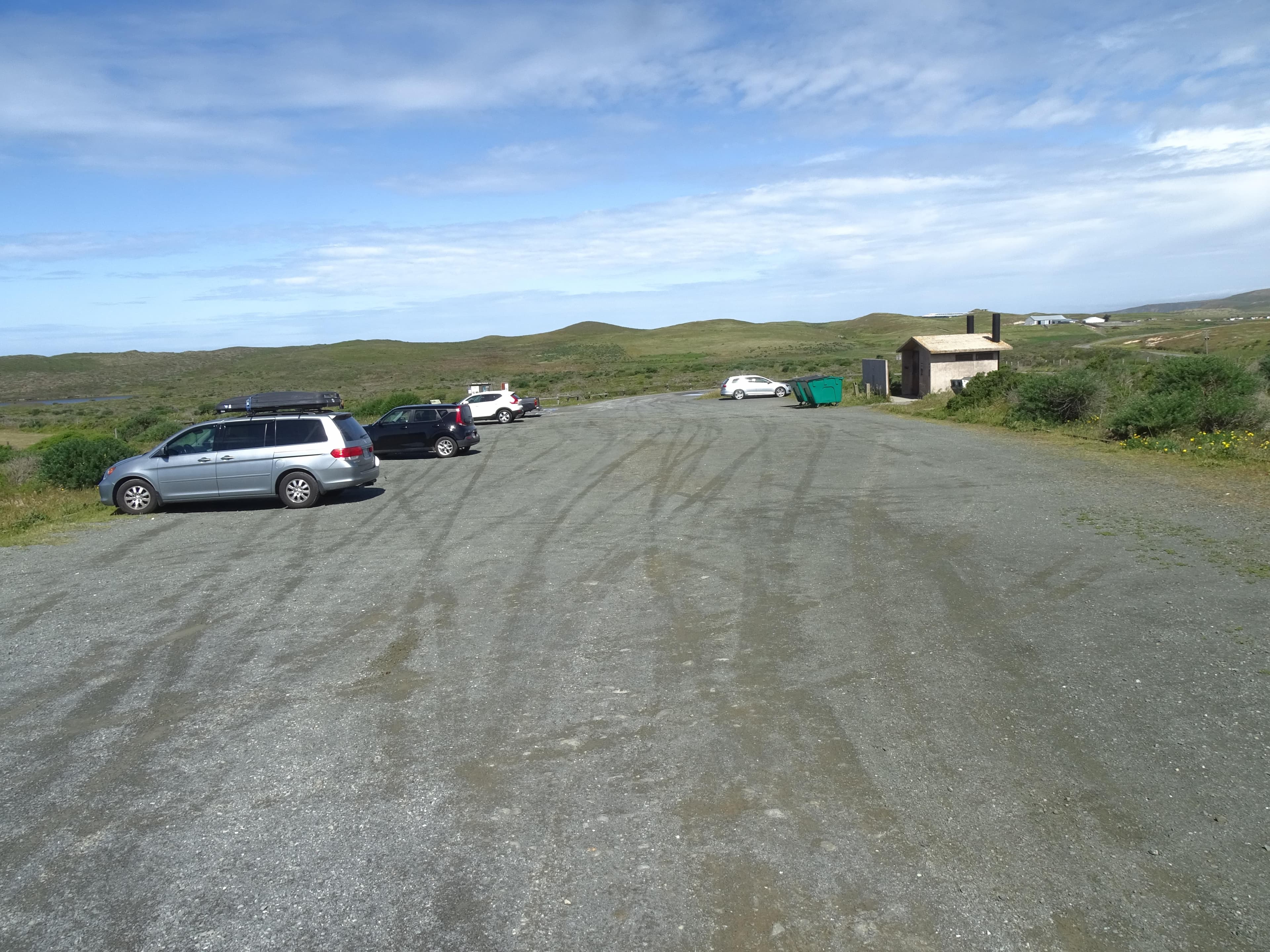 Five vehicles are parked in a gravel lot that is surrounded by grasslands.