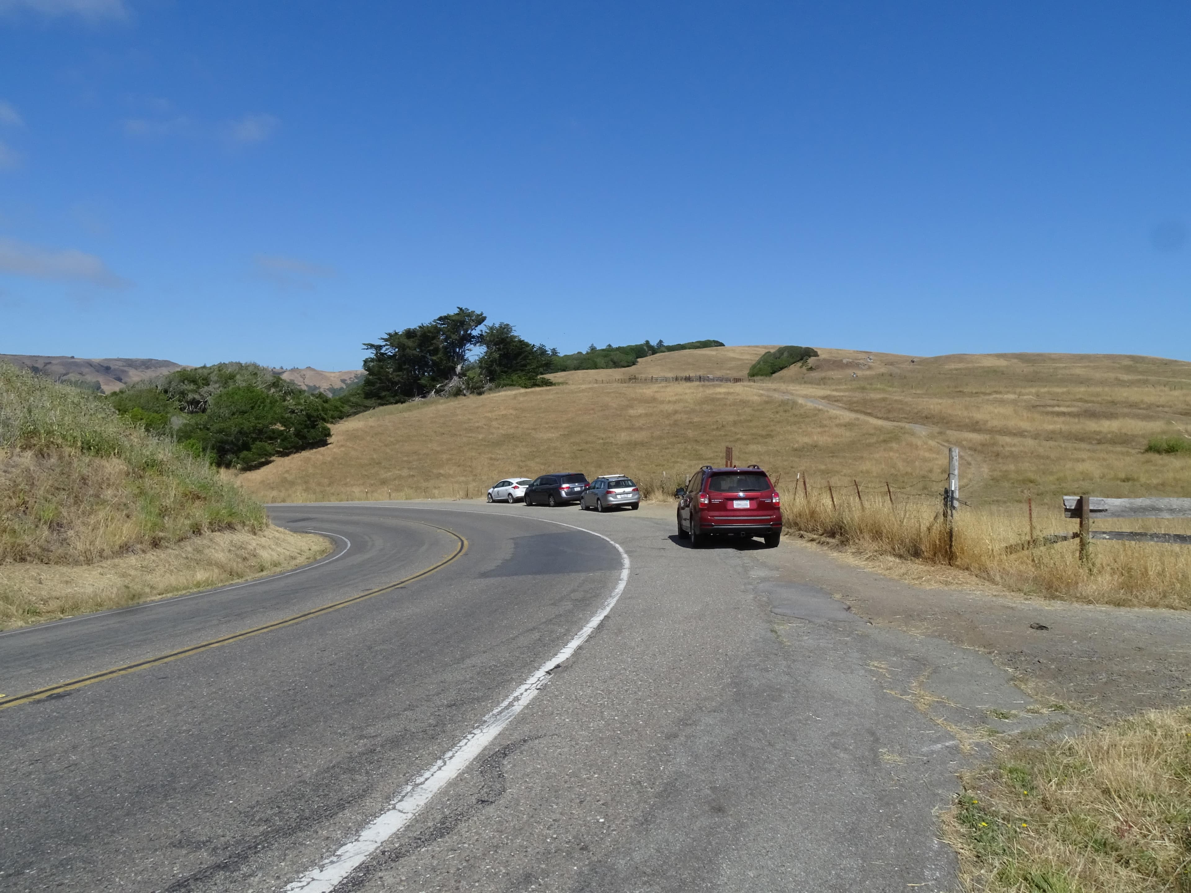 Four vehicles parked along a two-lane road that passes through pastureland.