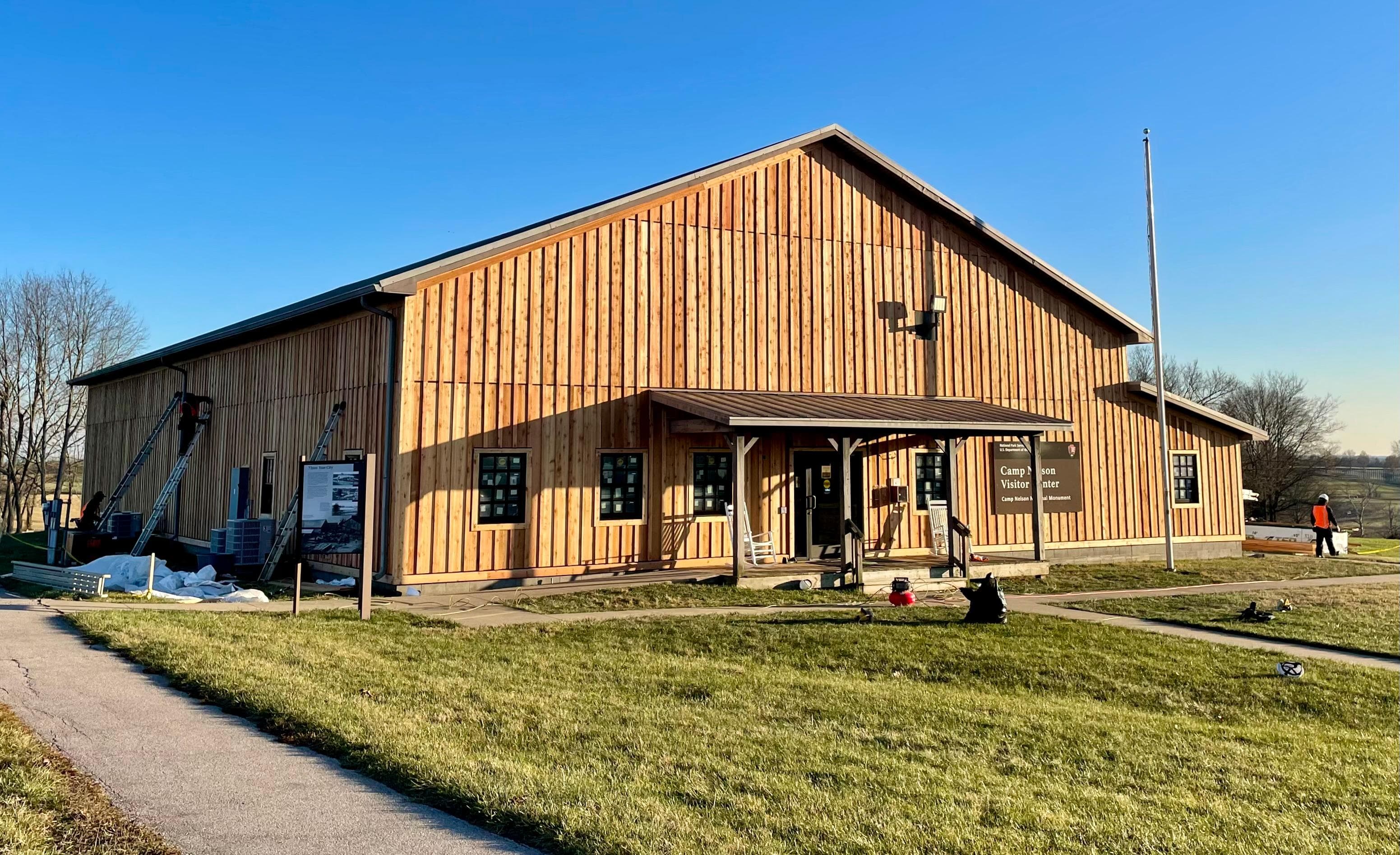 A wooden building surrounded by grass and a pave cement path.