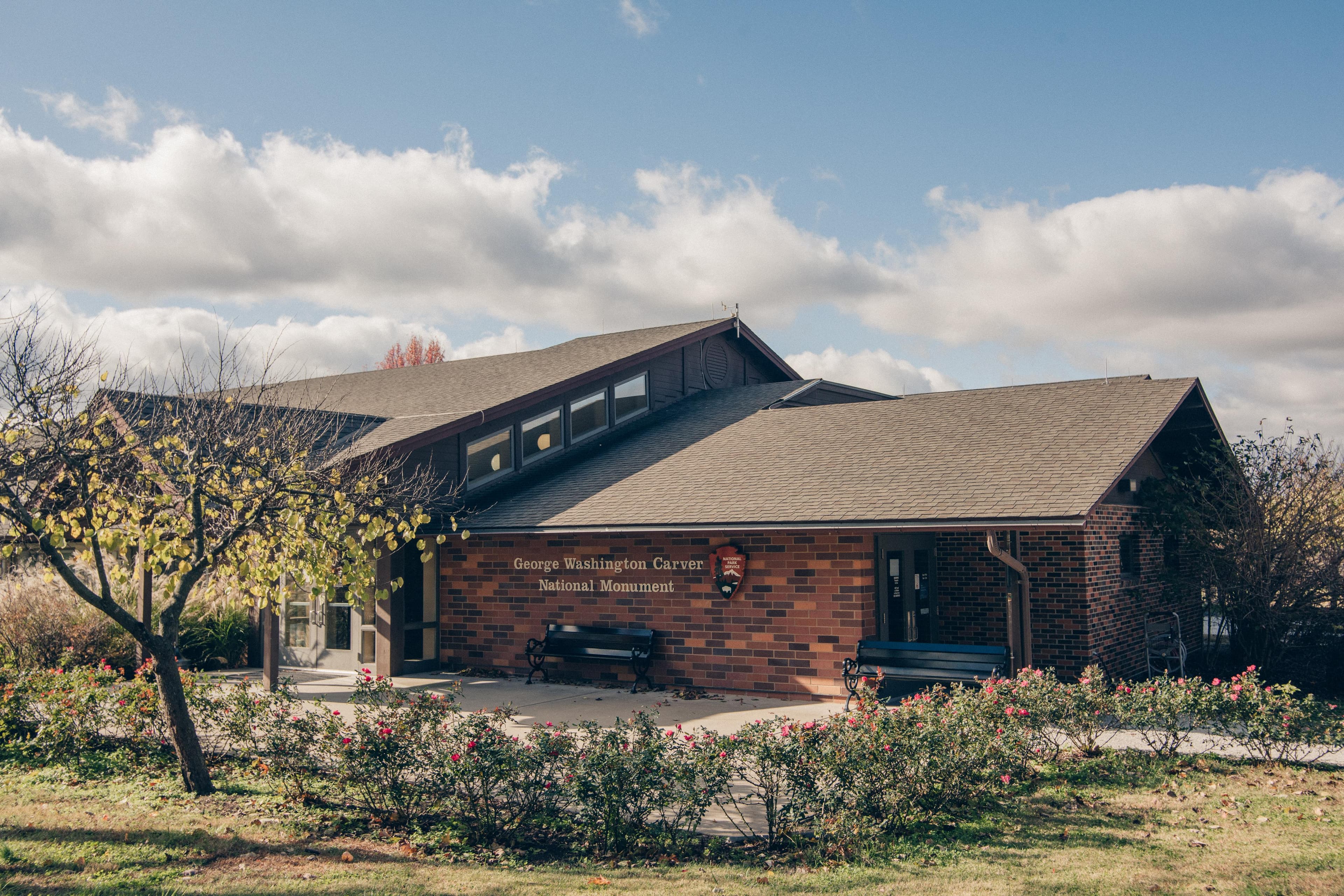 A brick building with landscape and a black bench.