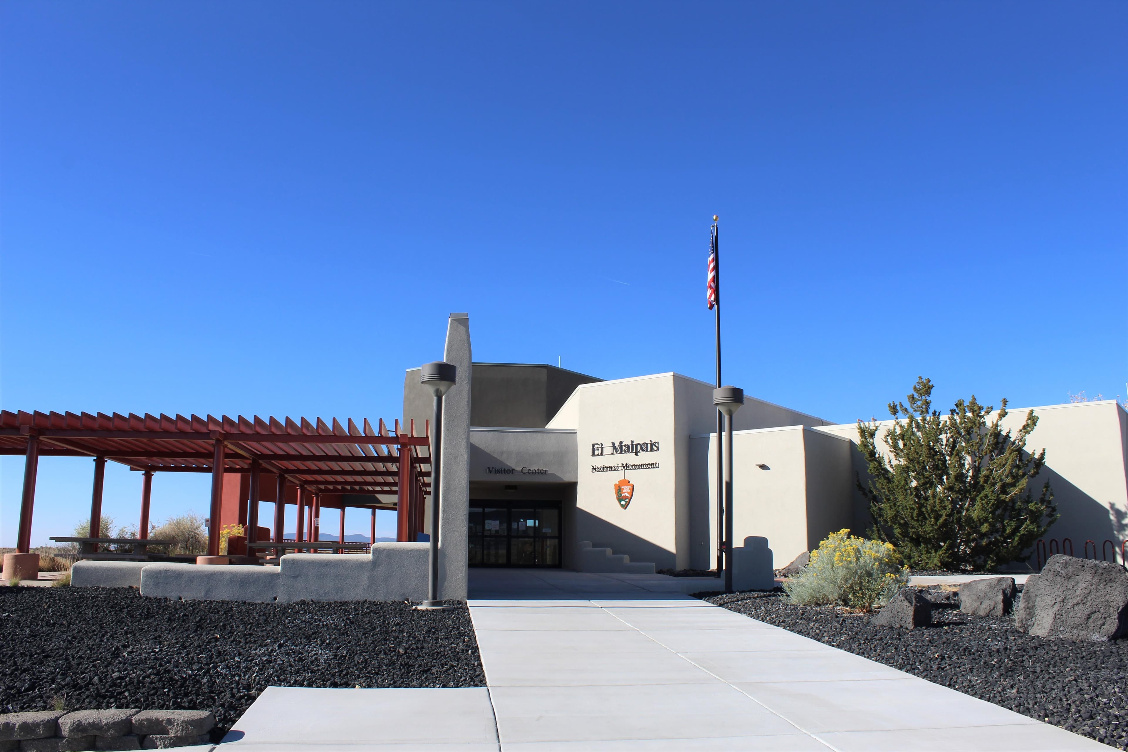 a sidewalk leads to a gray stucco, adobe-style visitor center
