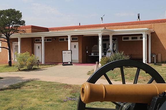 adobe building with porch in front and cannon on grass in front