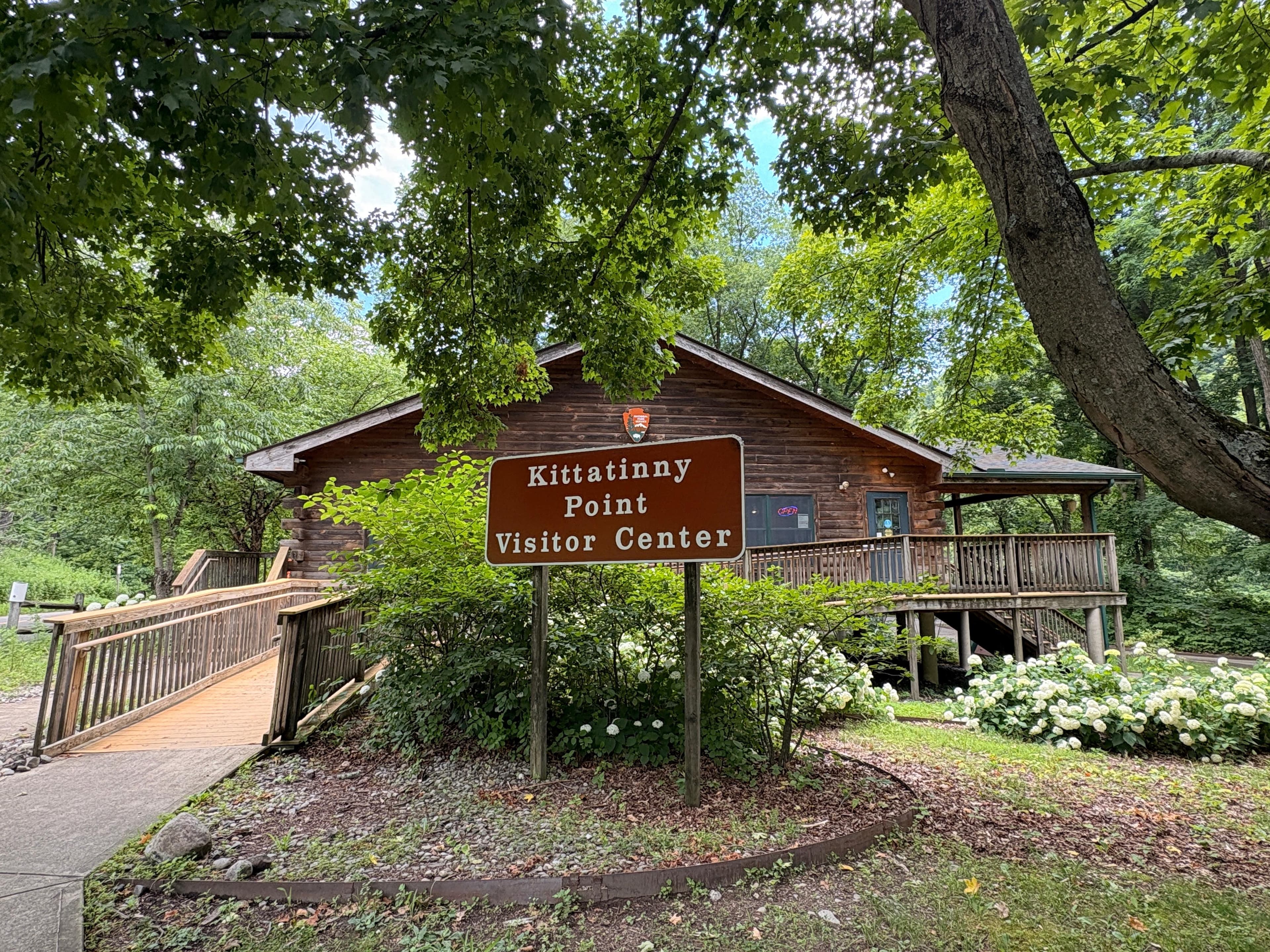 A wood log building with a ramp. A sign in front says Kittatinny Point Visitor Center.