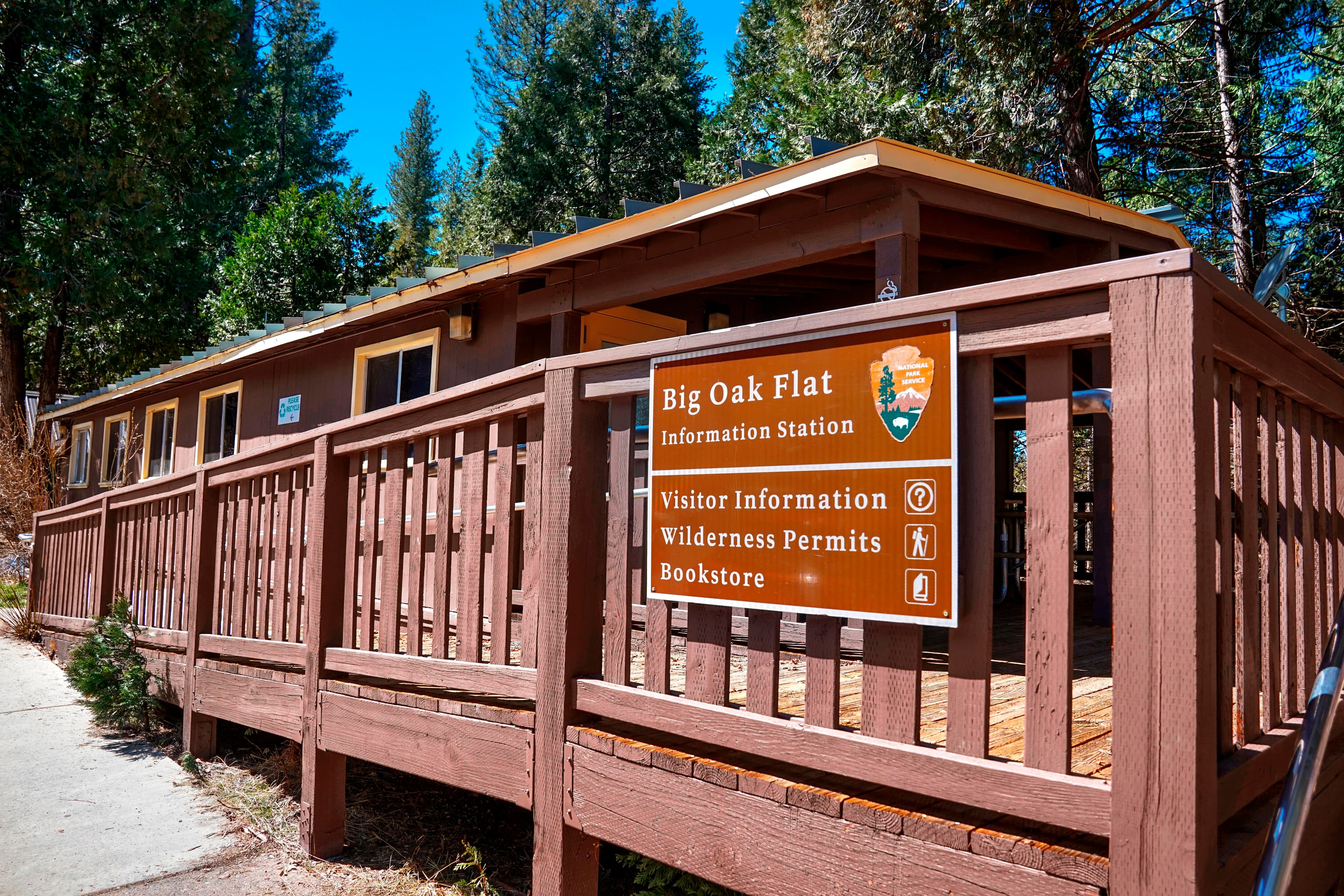A brown wooden building with a fenced deck has a sign that reads Big Oak Flat Information Station.