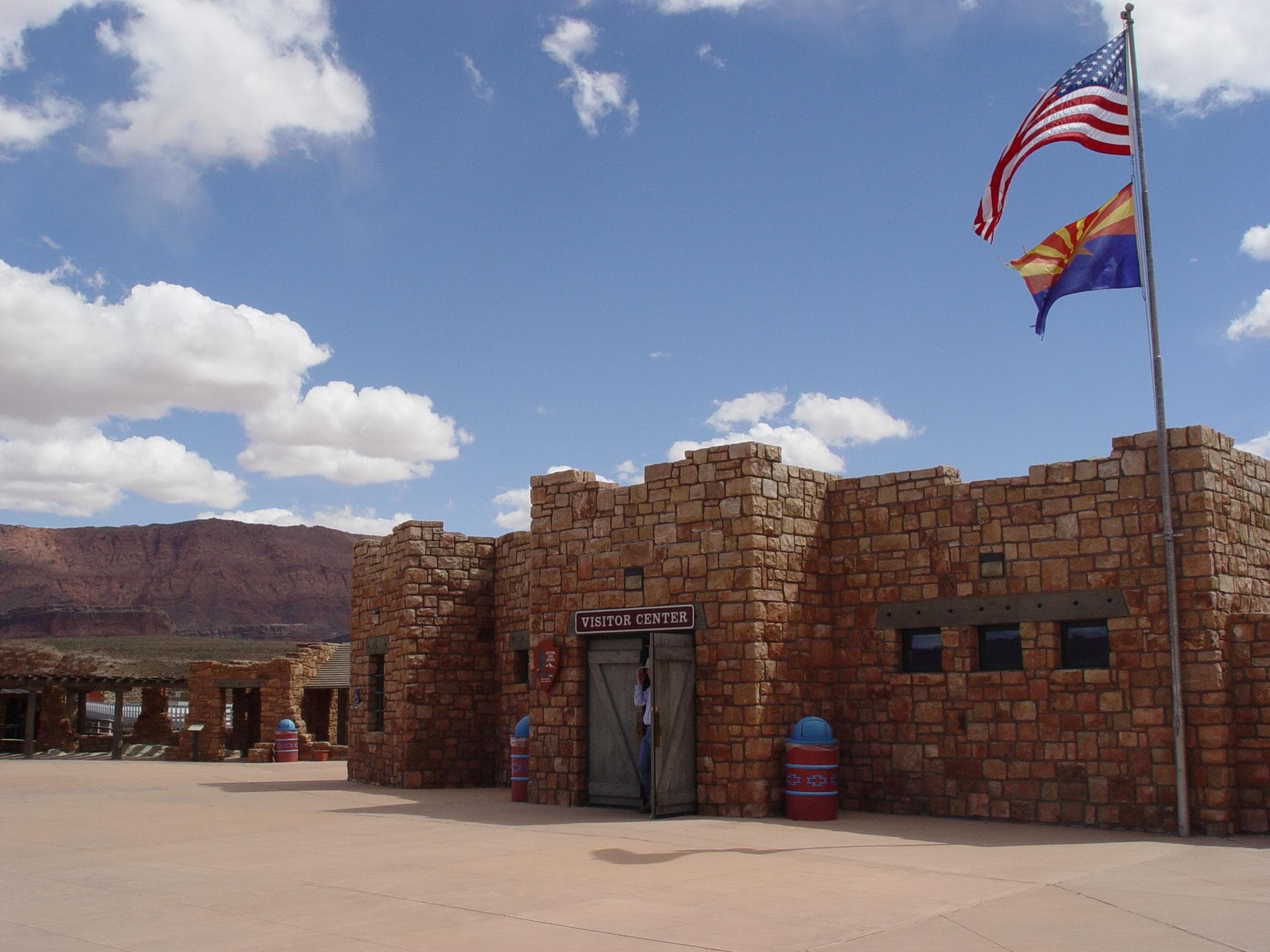 Rock mortar building with wooden doors. Arizona and United States flag on pole in front.