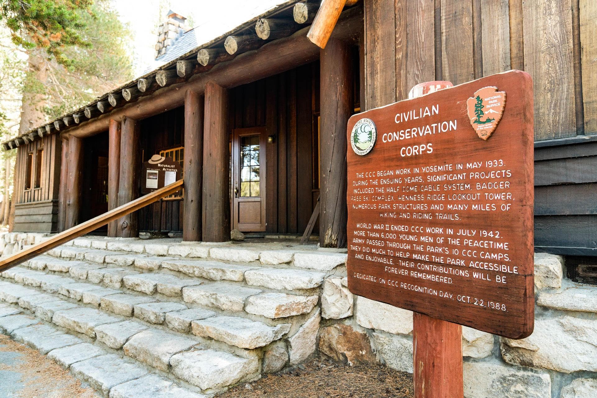 Stone steps lead to the covered porch of a stone building. A large brown wooden sign is in front.