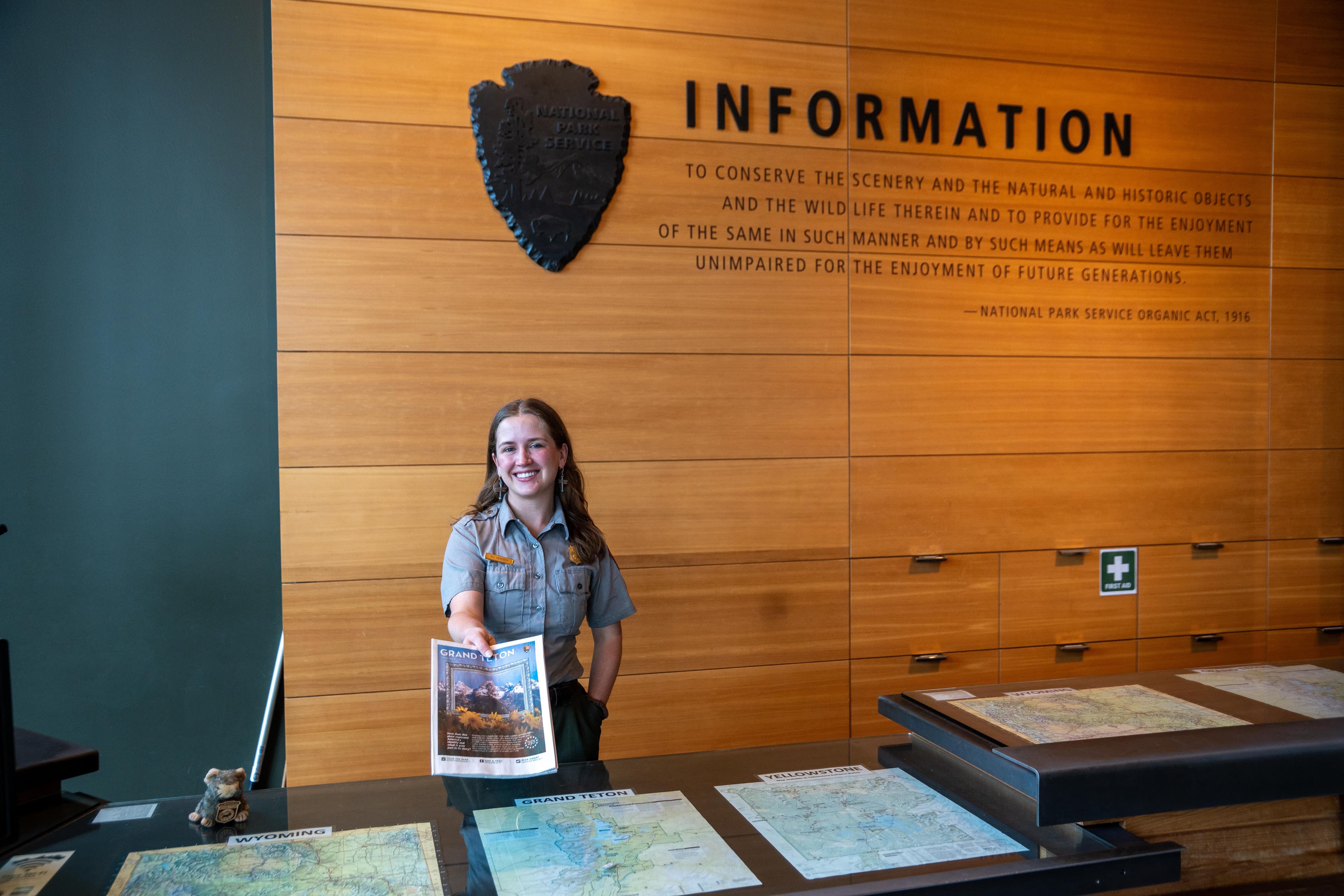 A Ranger standing behind an information desk and holding out a newspaper guide