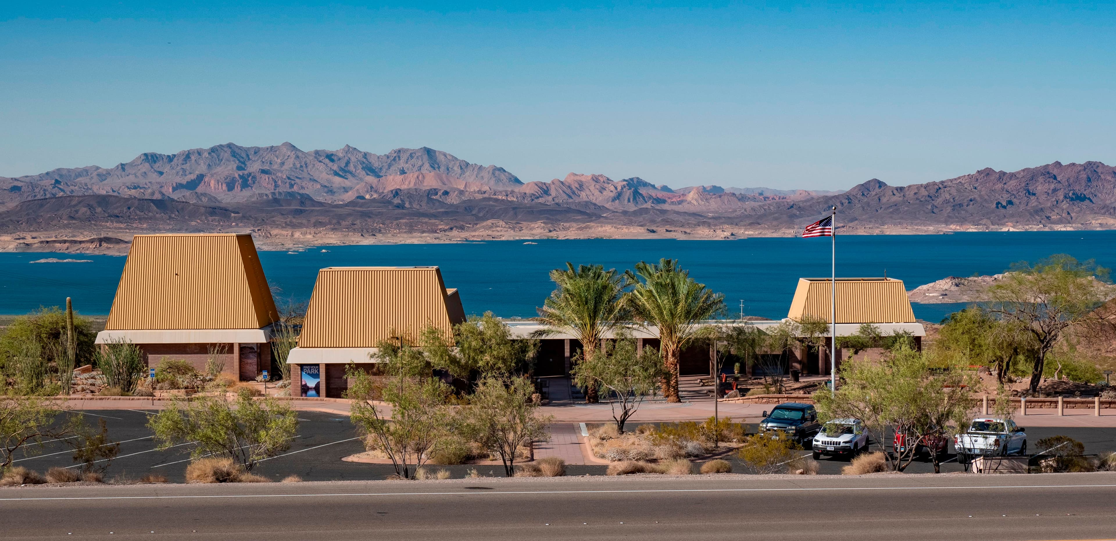 Large tan building in the desert with a blue lake in the background.